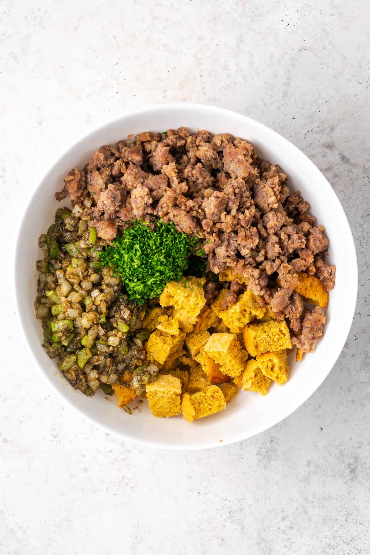 Cornbread cubes, fresh parsley, cooked sausage and vegetables in a large mixing bowl. 