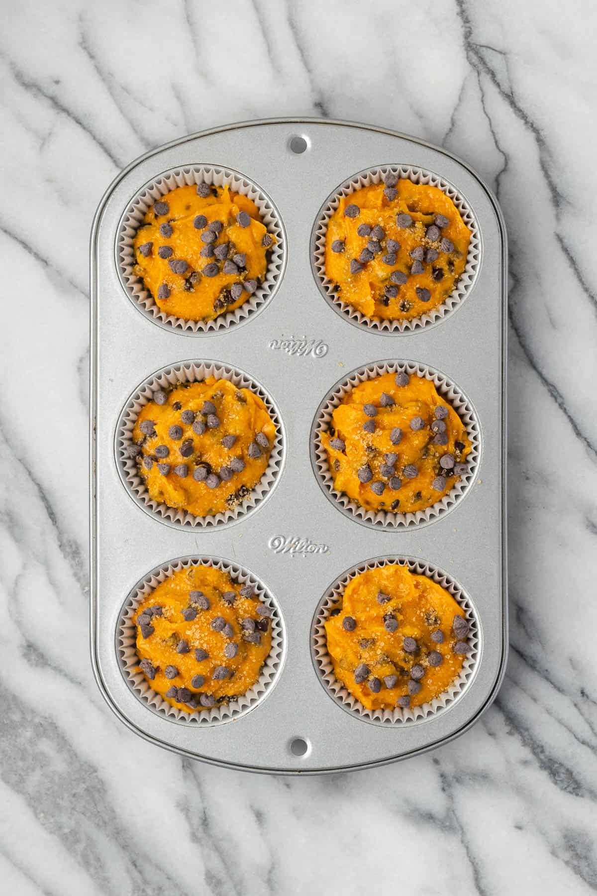 Unbaked pumpkin chocolate chip muffins in a baking tin sitting on a marble counter.