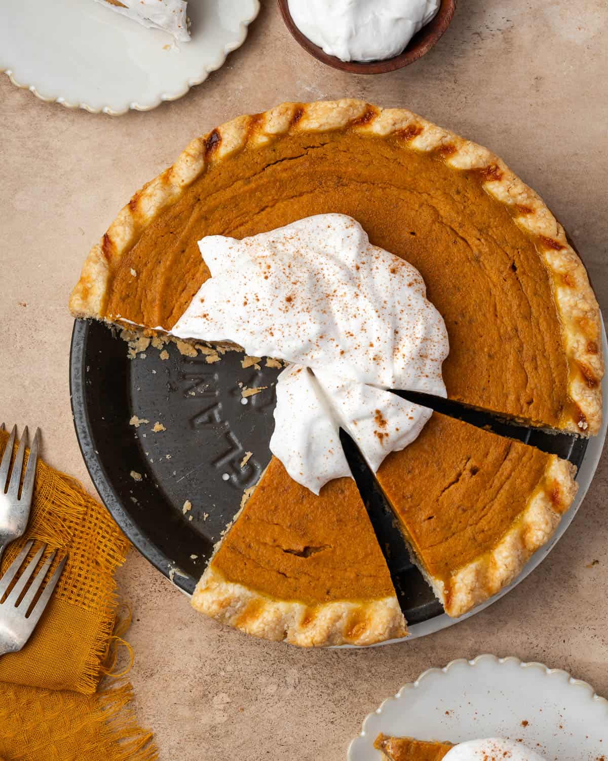 A gluten free pumpkin pie topped with whipped cream and cut into slices. 