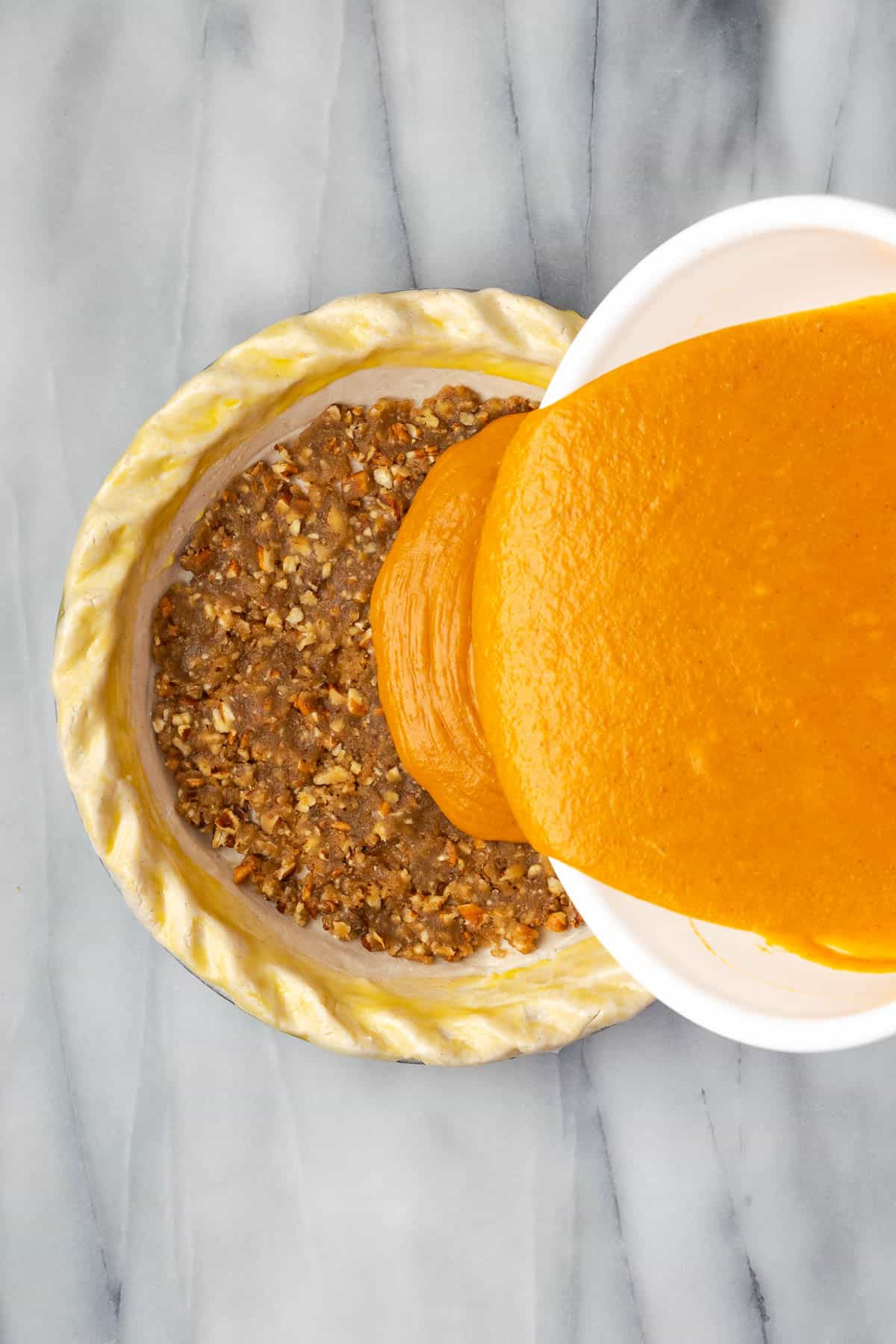 Pumpkin pie filling being poured into an unbaked pie shell. 