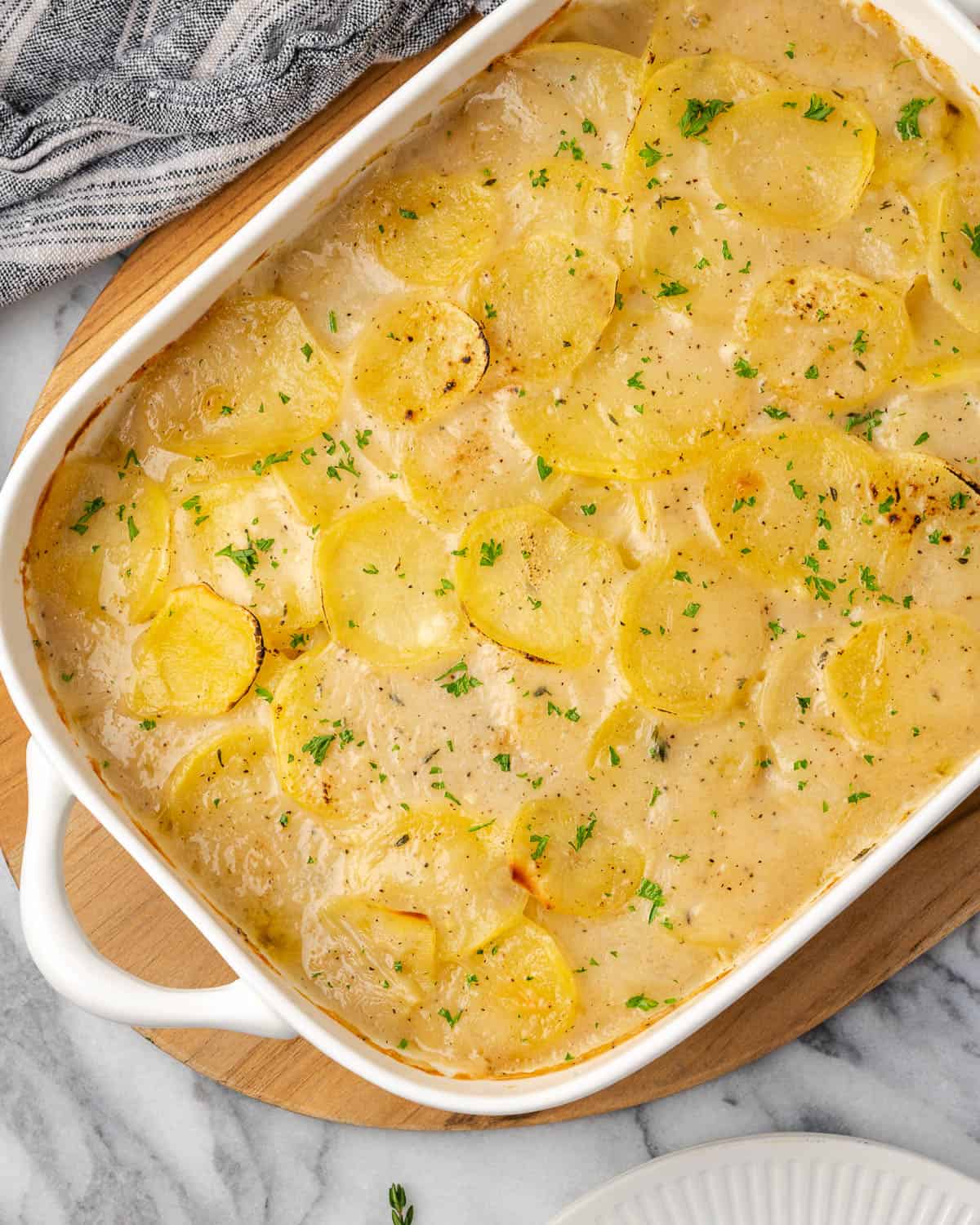 A baking dish of gluten free scalloped potatoes sitting on a marble counter.