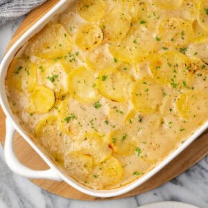 A baking dish of gluten free scalloped potatoes sitting on a marble counter.