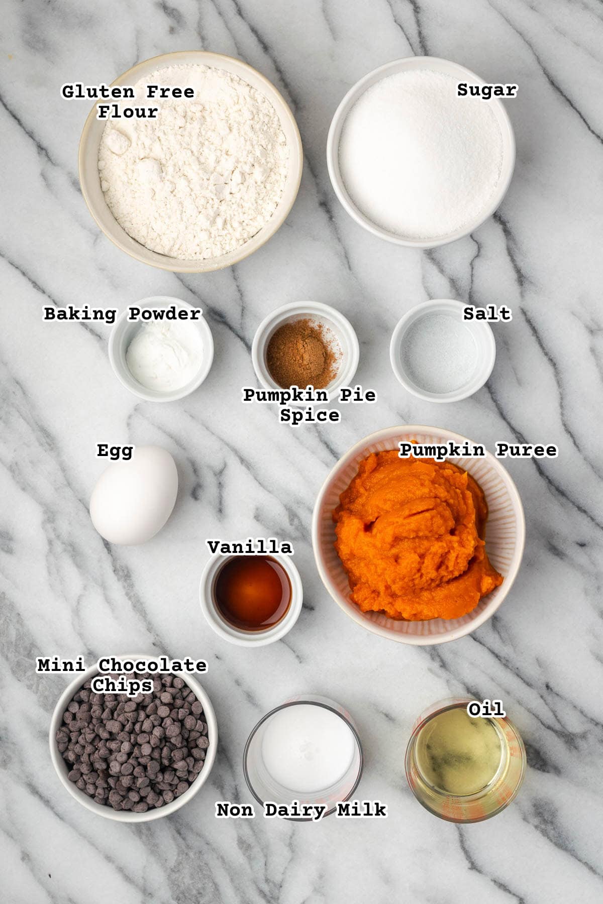 Ingredients for gluten free pumpkin chocolate chip muffins sitting on a marble counter.
