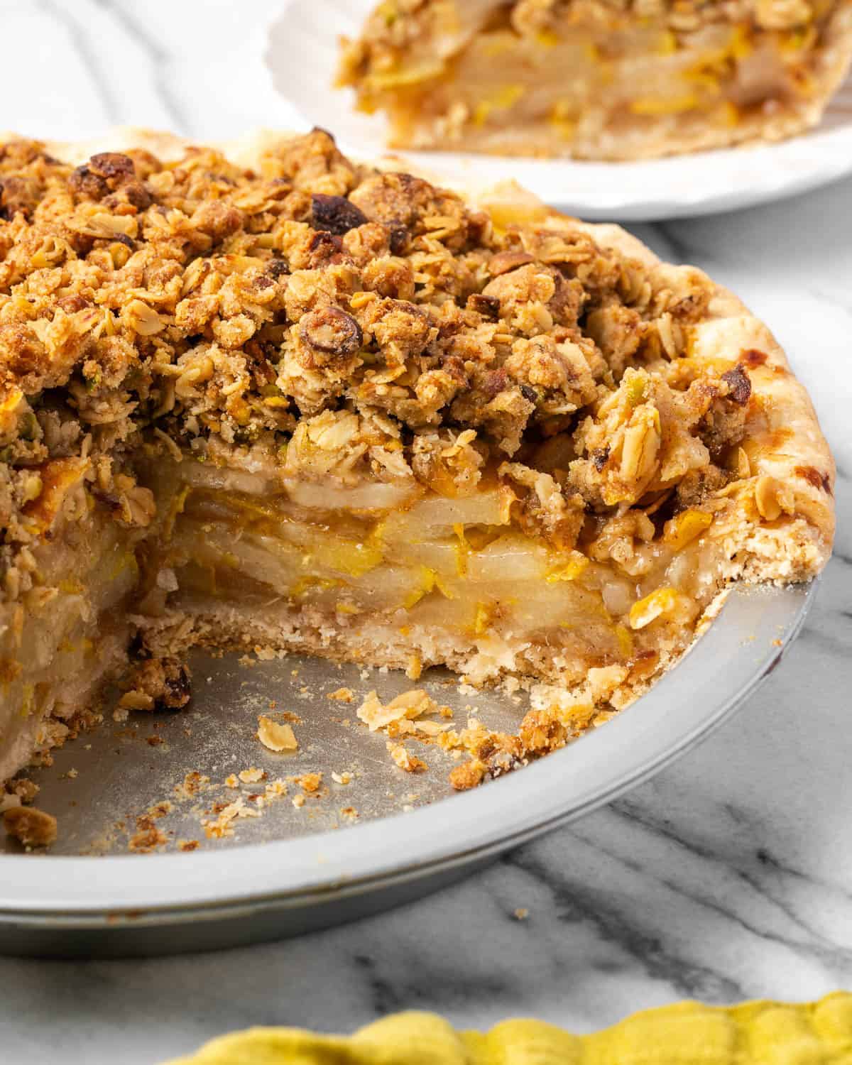 A sliced pear crumble pie in a pie plate sitting on a marble counter.