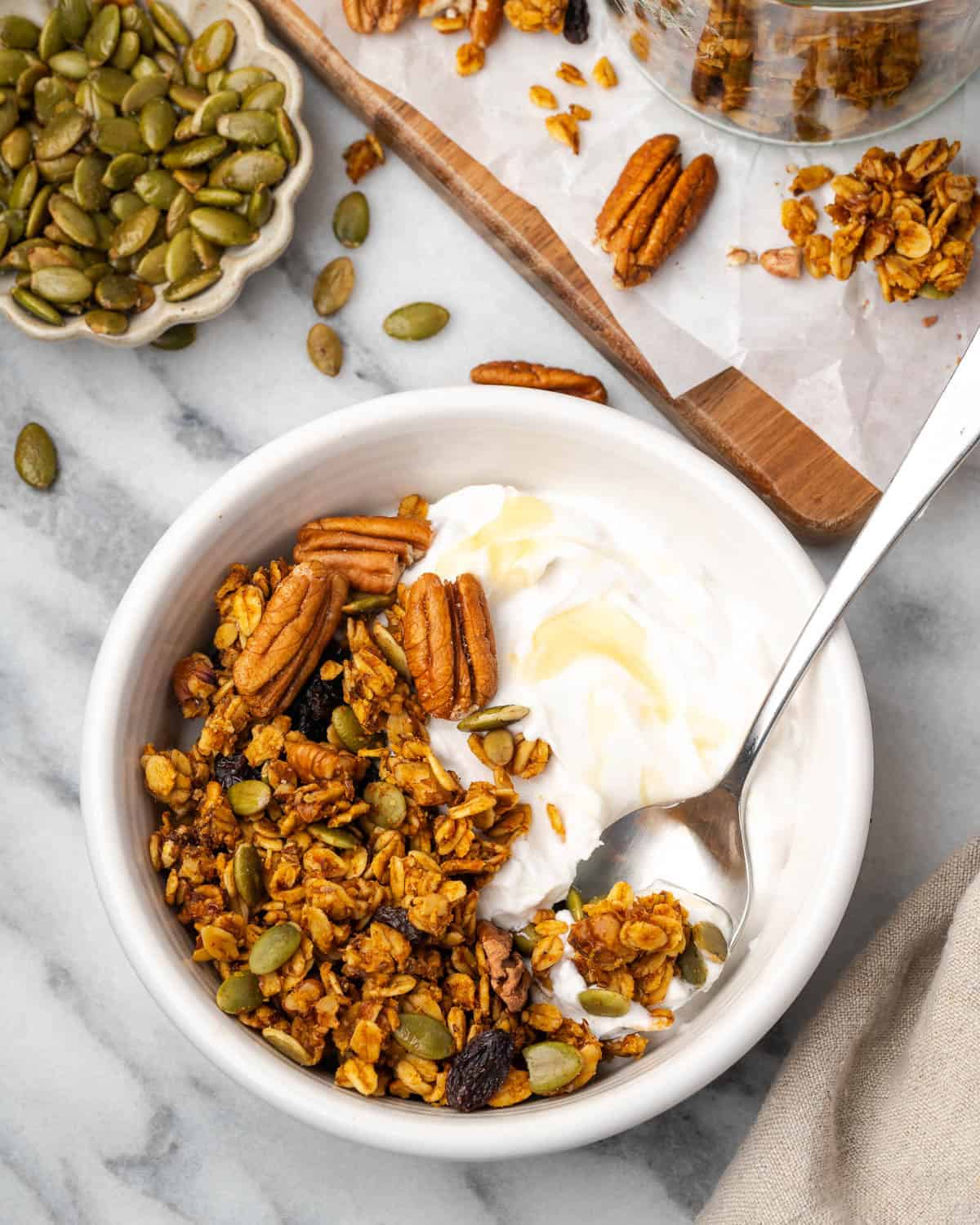 Pumpkin seed granola served with a bowl of yogurt sitting on a marble counter.