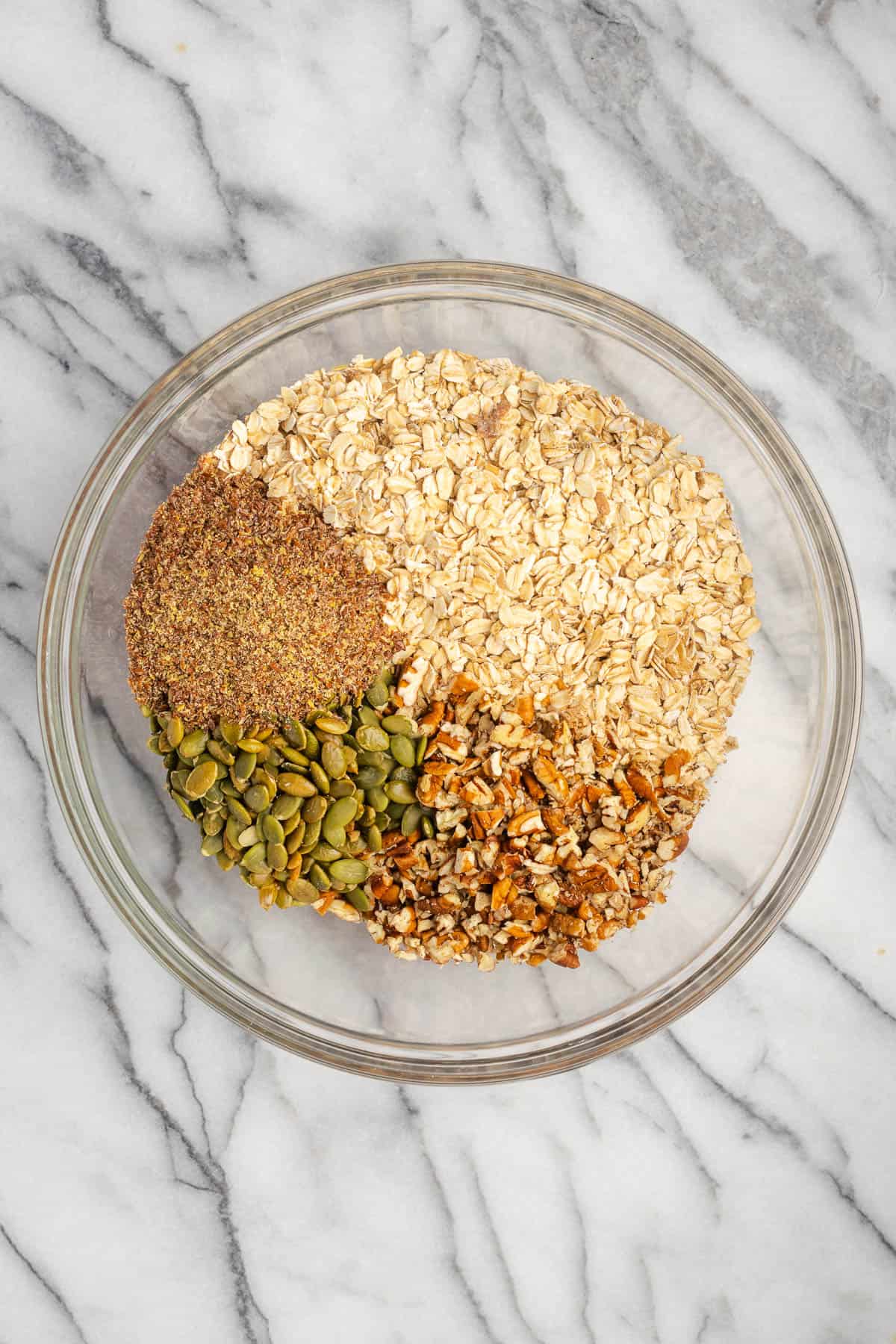 Oats, flax, pecans, and pumpkin seeds combined in a large mixing bowl. 