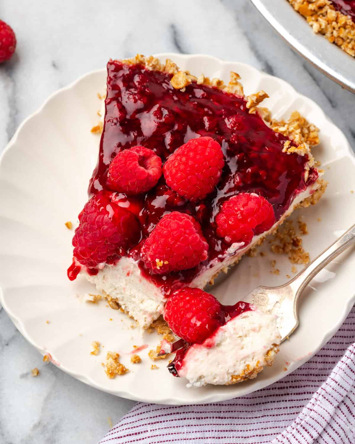 A slice of raspberry cream pie with a bite taken out on a small dessert plate.