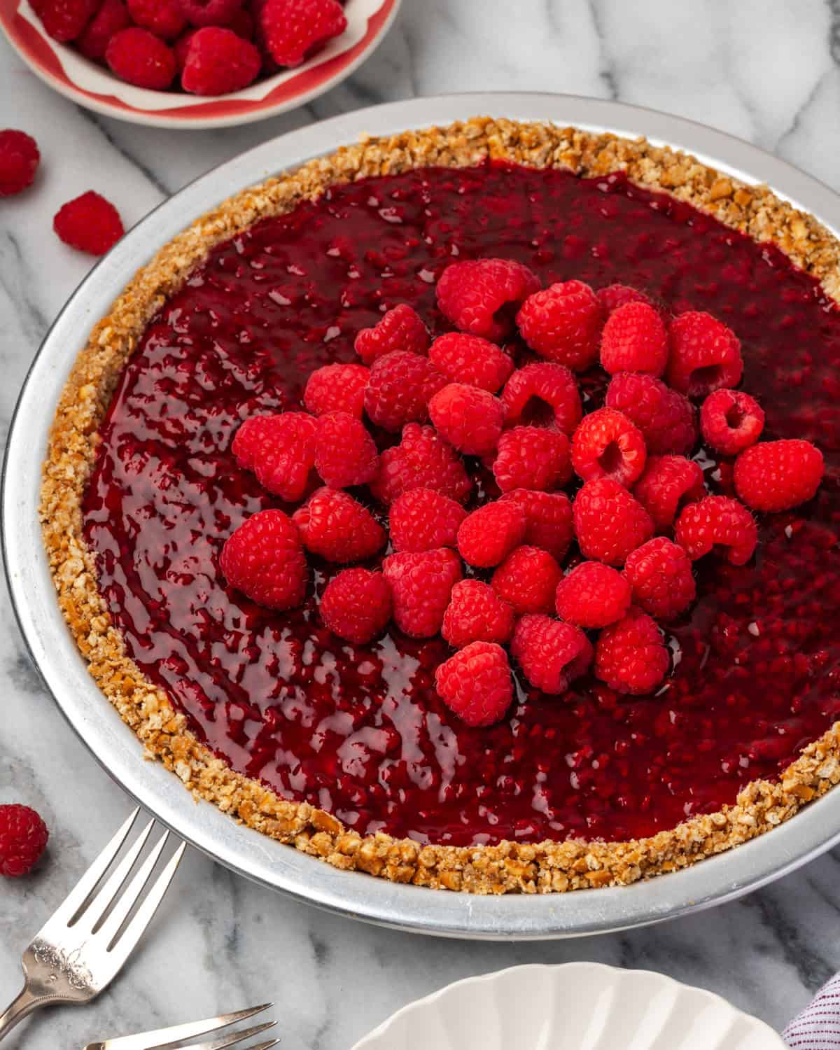 A raspberry cream pie sitting on a marble counter next to a small bowl of fresh berries. 