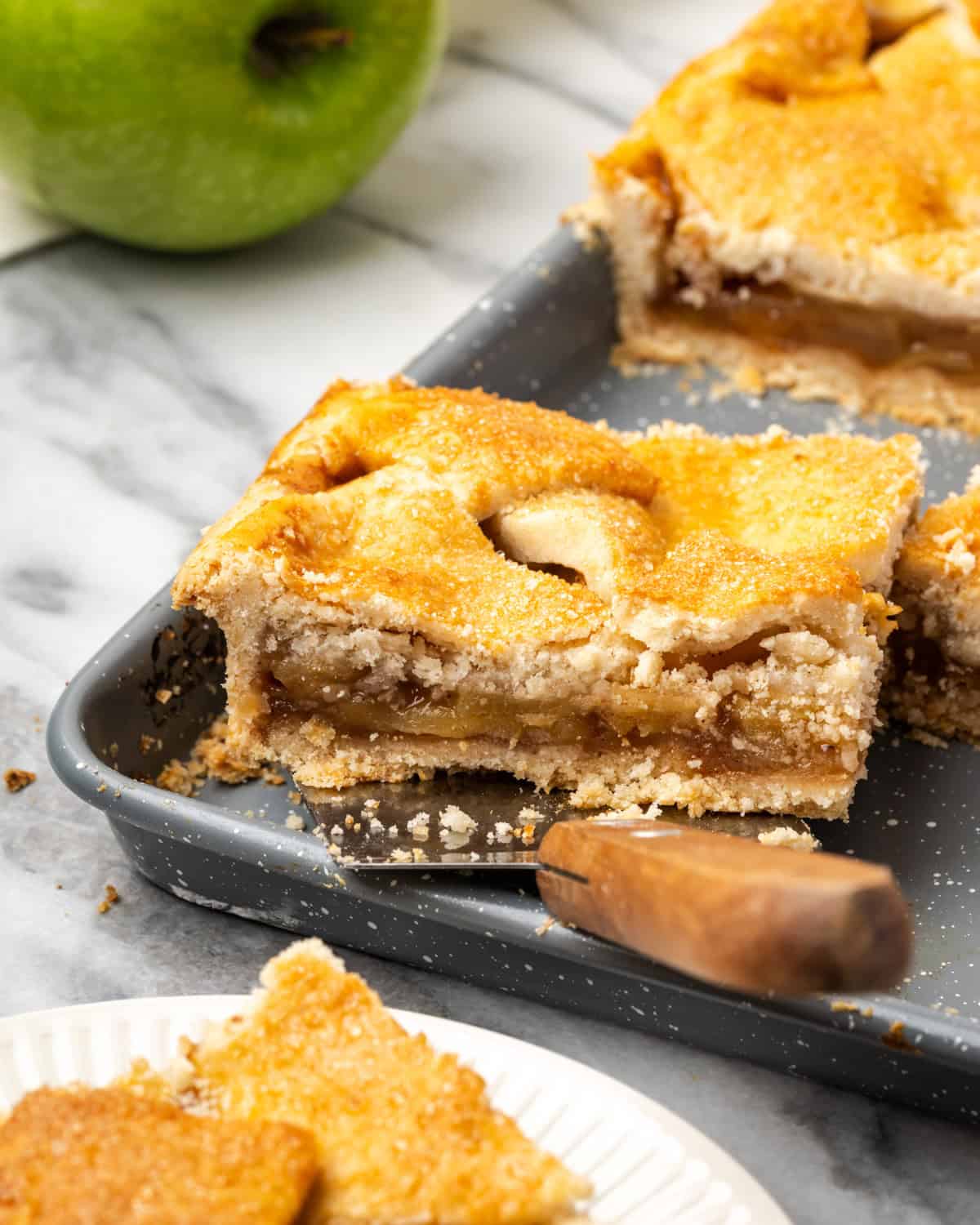 A square cut from an apple slab pie being lifted from the baking pan. 