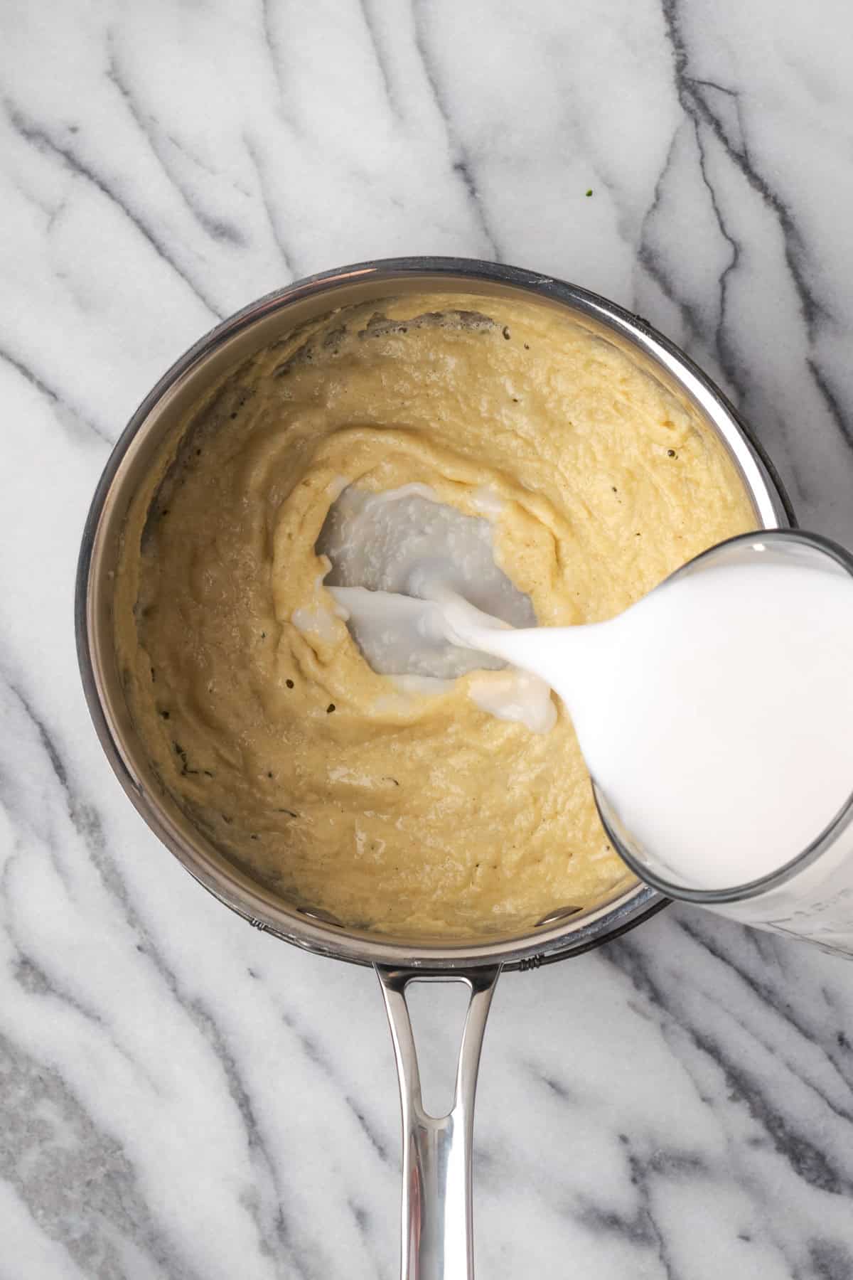 Milk being poured into the cooked roux in a saucepan. 