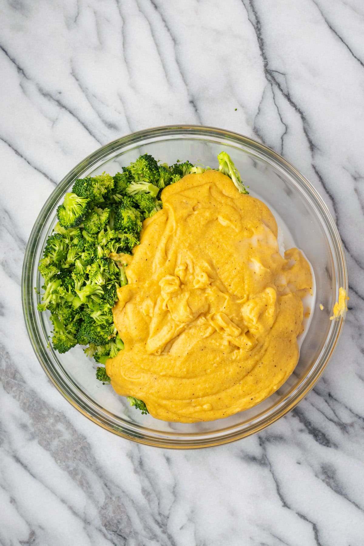 Vegan cheese sauce poured over broccoli and rice in a large mixing bowl. 