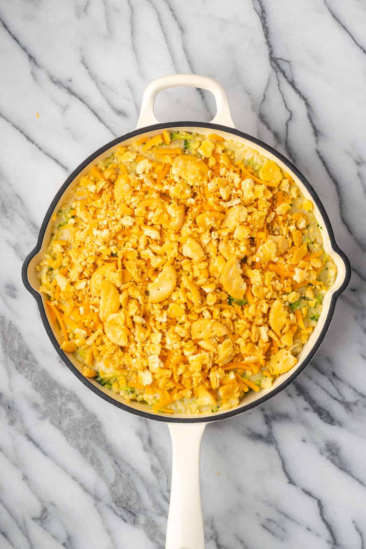 An unbaked broccoli rice casserole topped with shredded cheese and crushed crackers. 