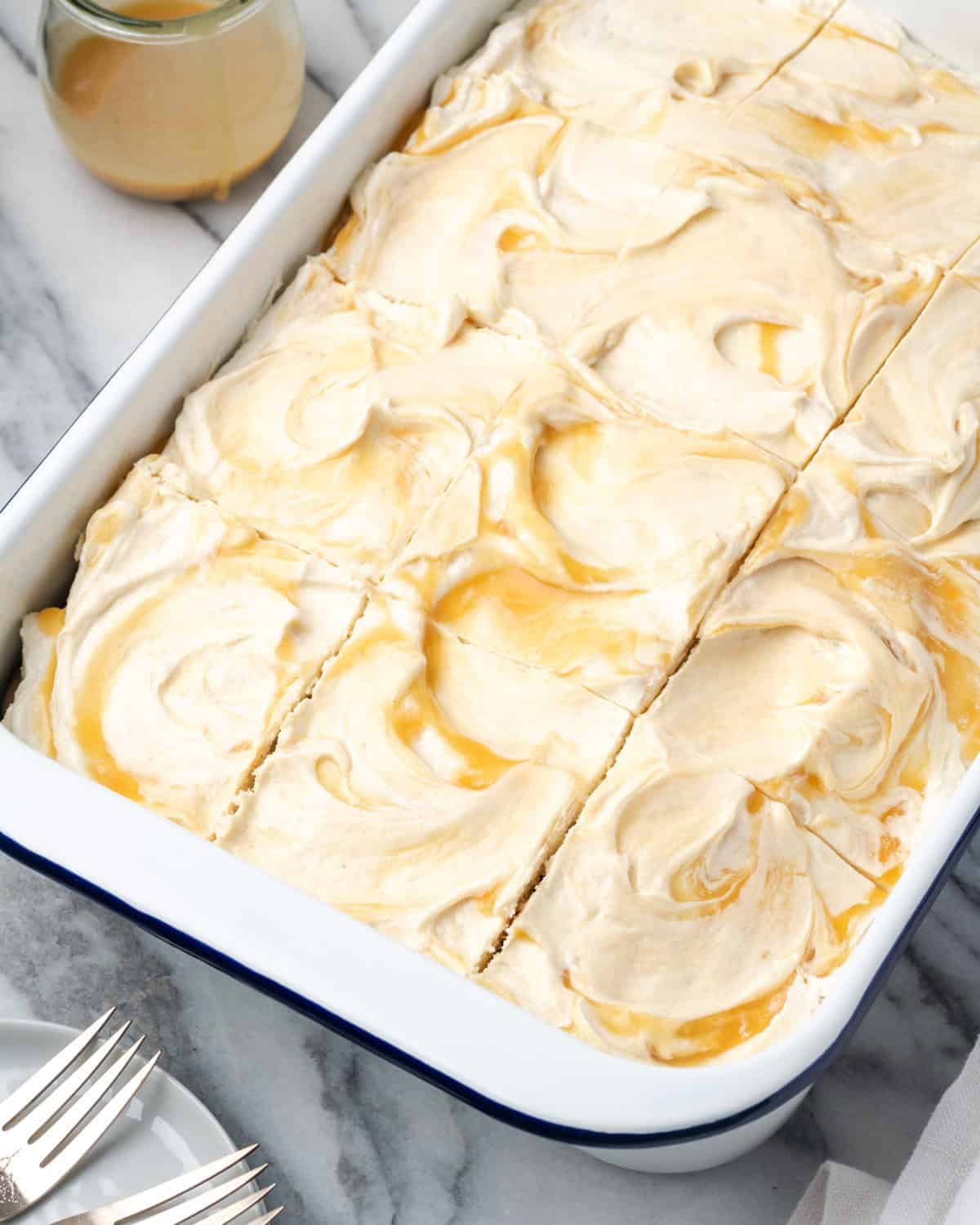 A sliced chocolate caramel poke cake served in a white baking dish. 
