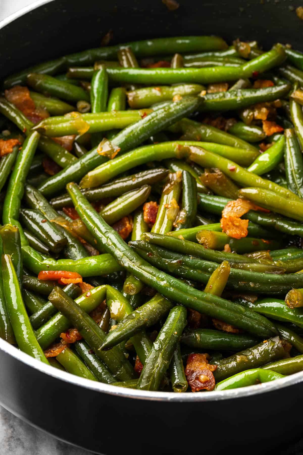 Green beans with bacon and onion cooking in a large saucepan.