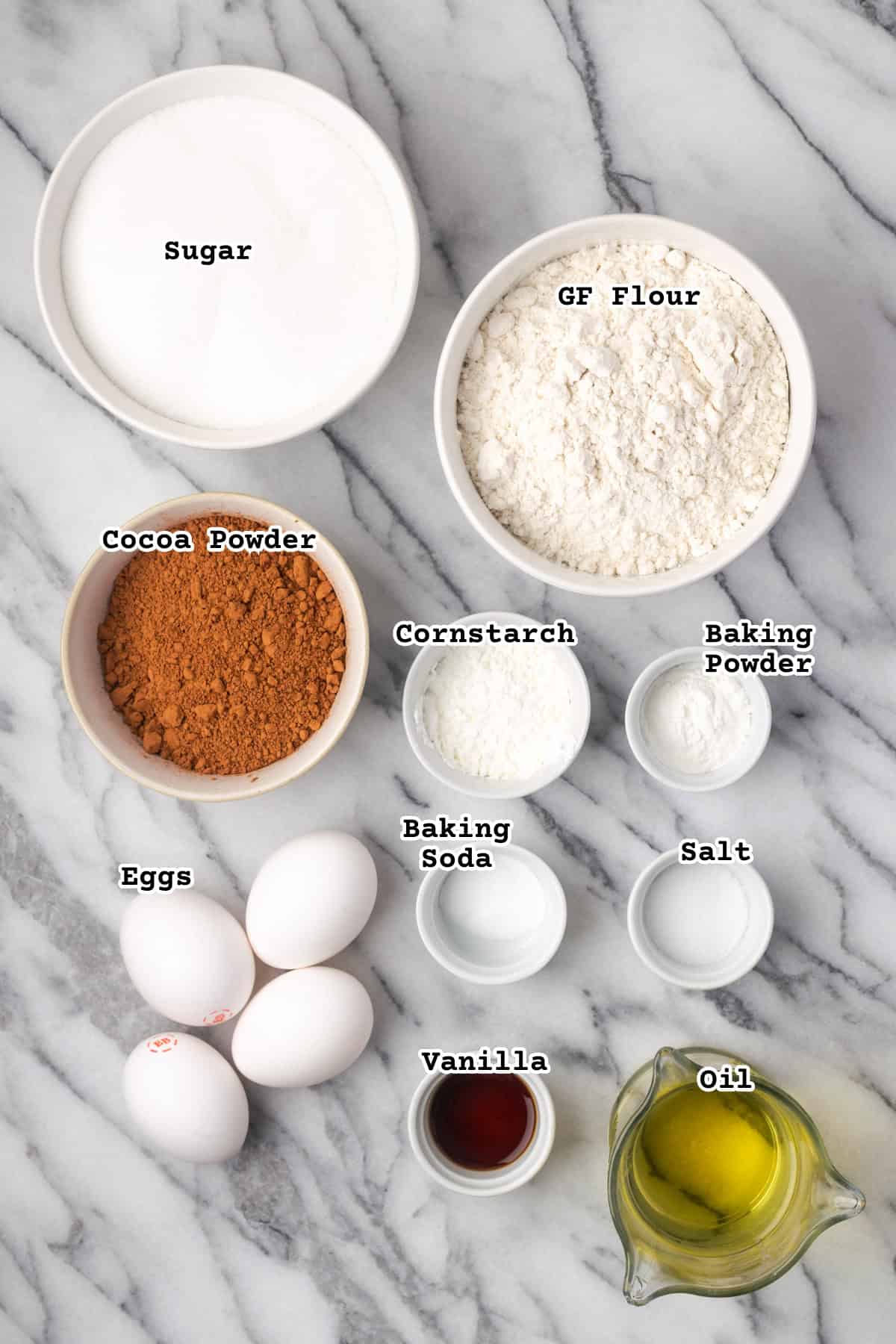 Ingredients for a chocolate cake sitting on a marble counter. 