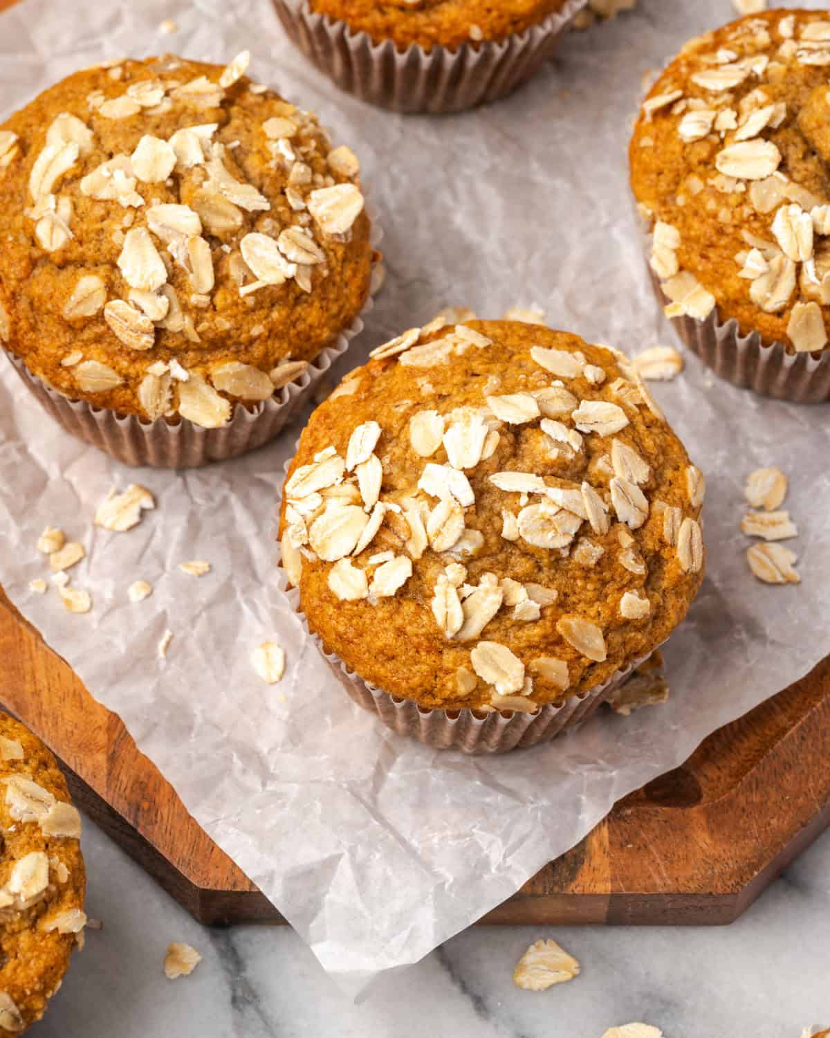 Several oat flour banana muffins on a wood serving tray.