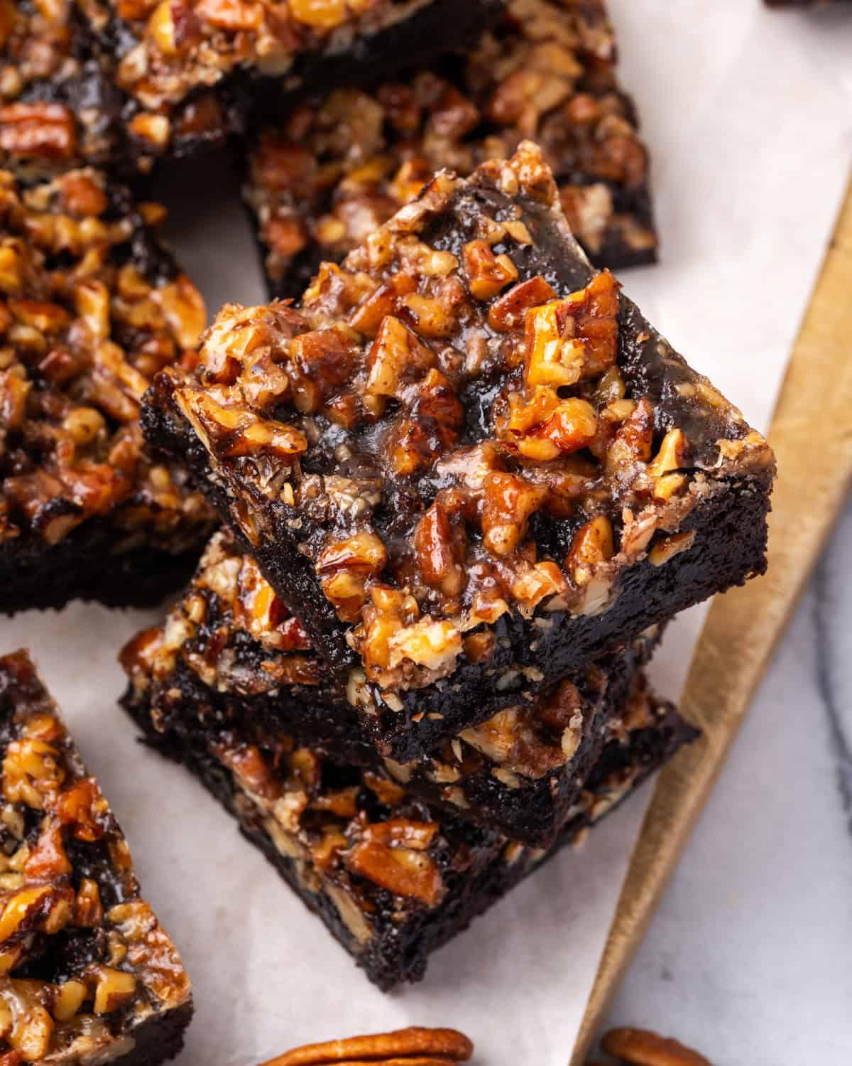 Three pecan pie brownies stacked up on a cutting board.