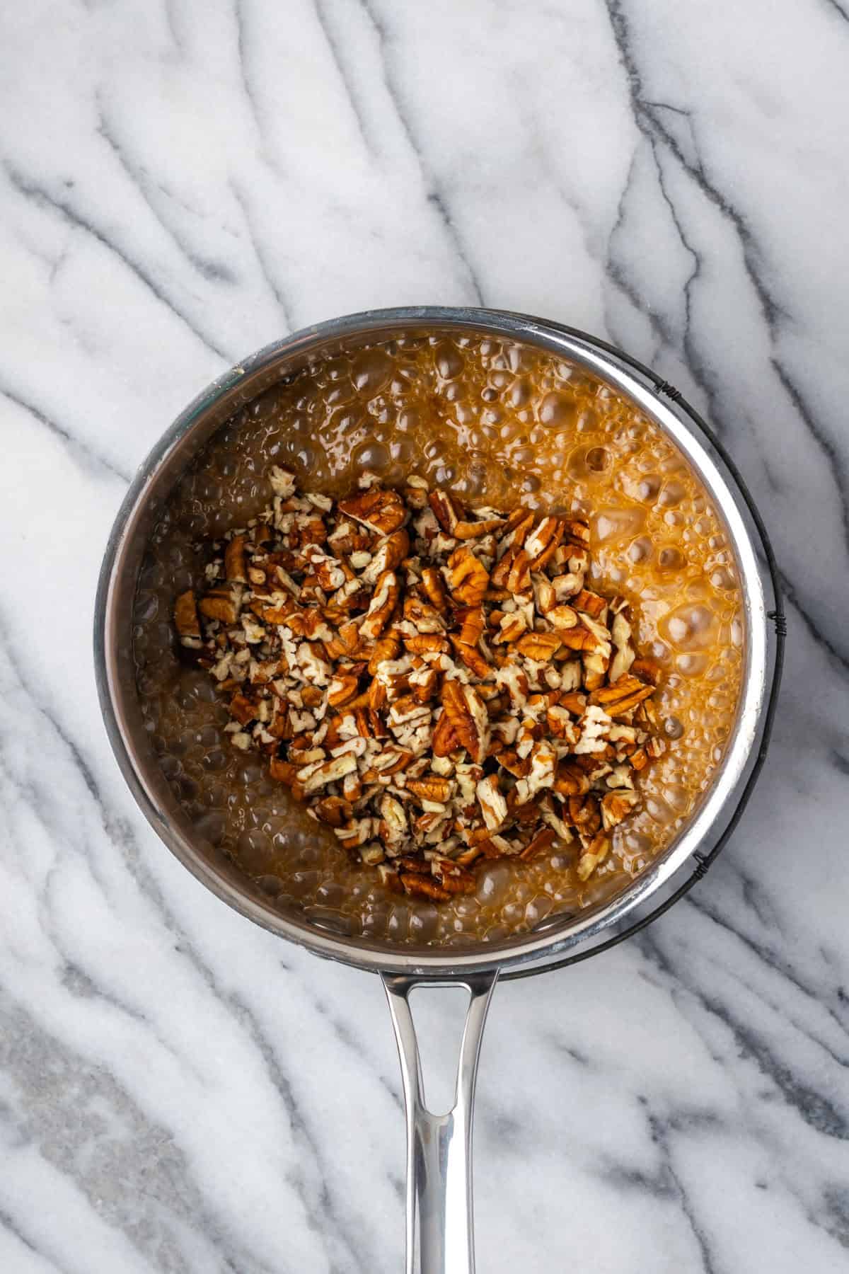 Chopped pecans being stirred into the caramel mixture.