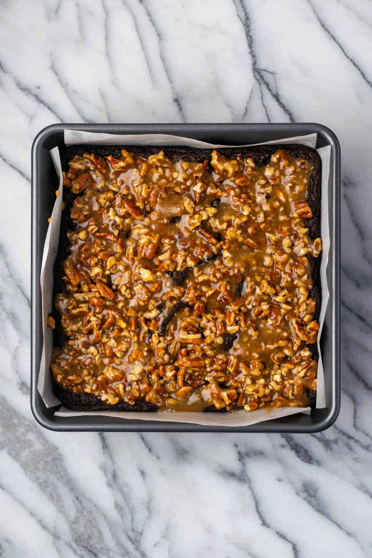Pecan pie mixture spread over a pan of partially baked brownies.