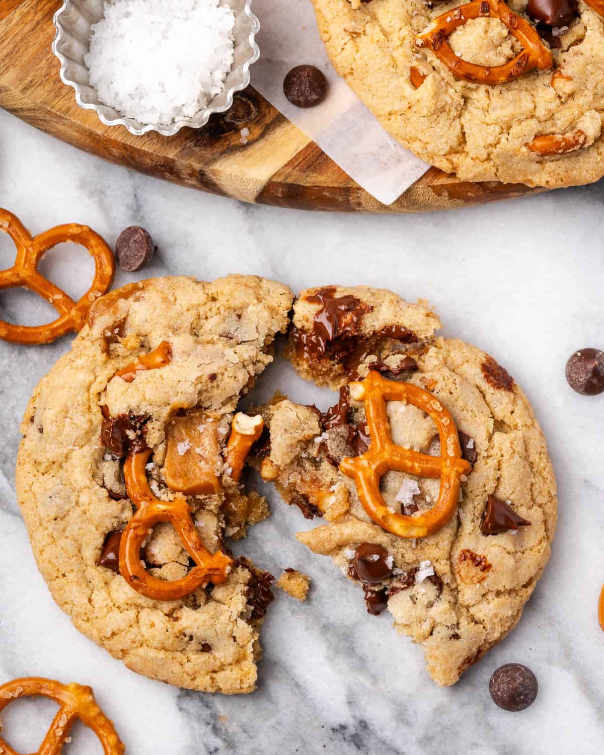 A caramel pretzel chocolate chip cookie broken in half showing the melted chocolate inside.