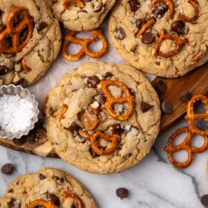 A batch of caramel pretzel chocolate chip cookies scattered on a wood tray.