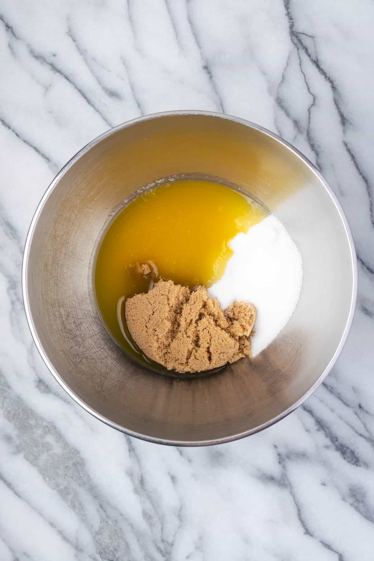 Granulated sugar, brown sugar and melted butter combined in a large metal mixing bowl.