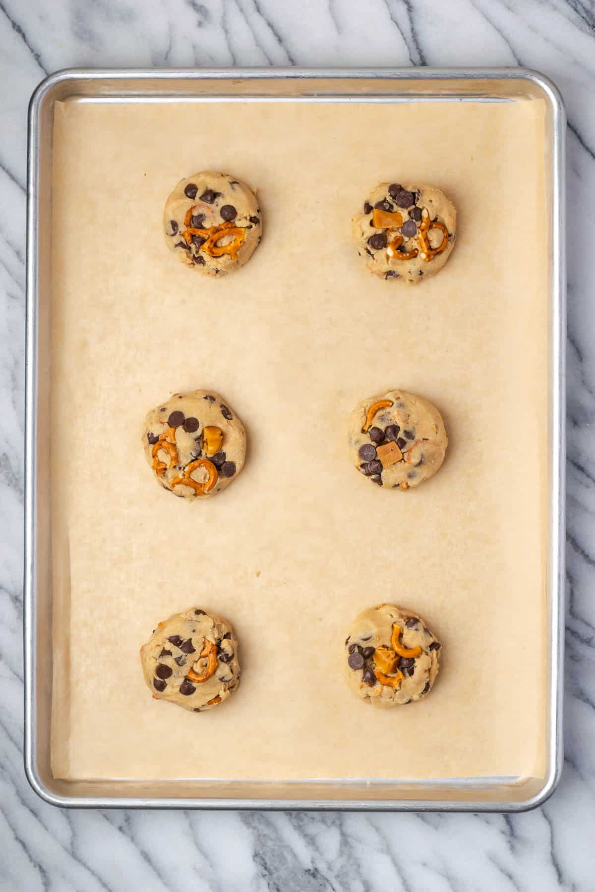 Six unbaked cookie dough balls on a large baking sheet.
