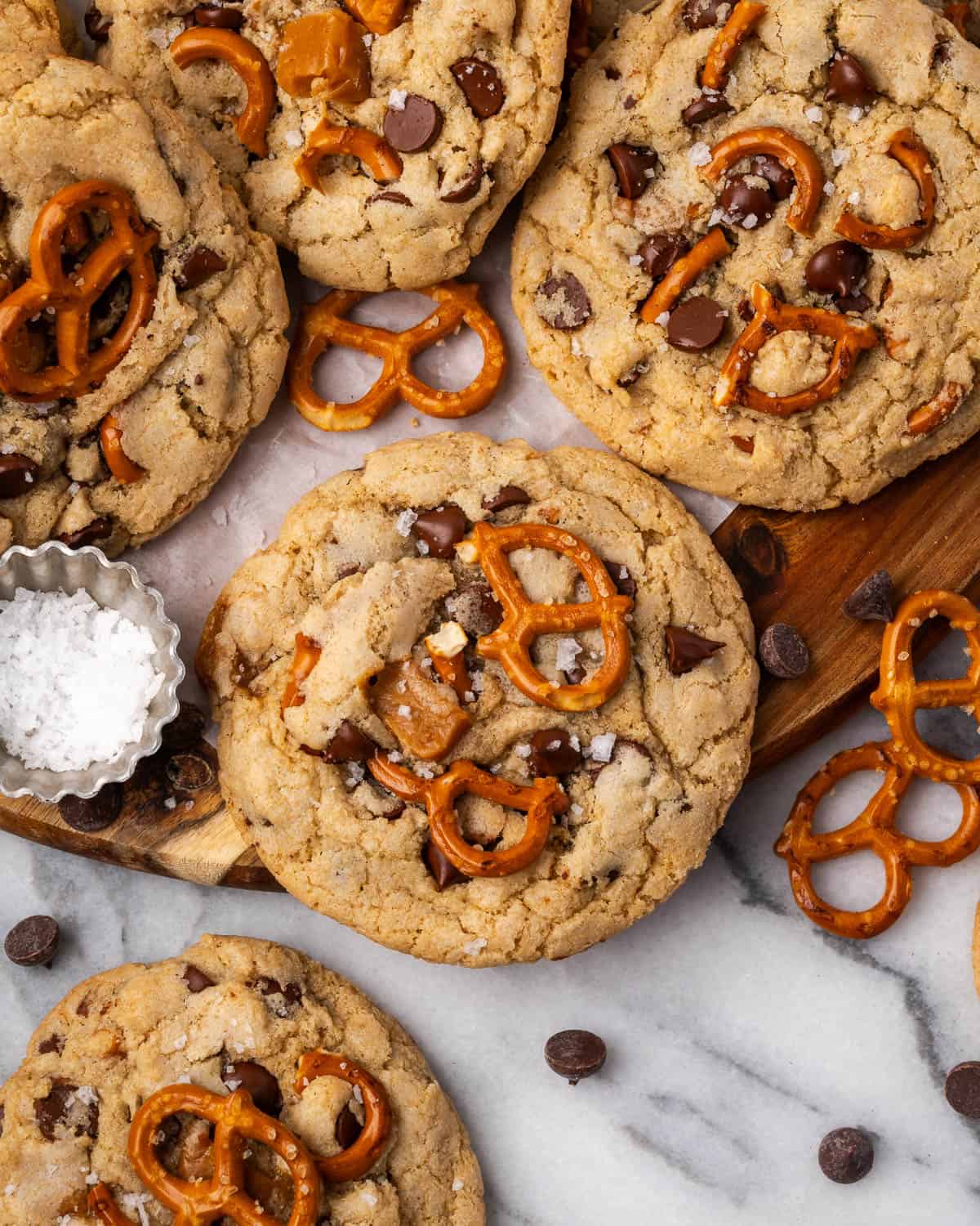 Several caramel pretzel chocolate chip cookies scattered on a wooden tray.