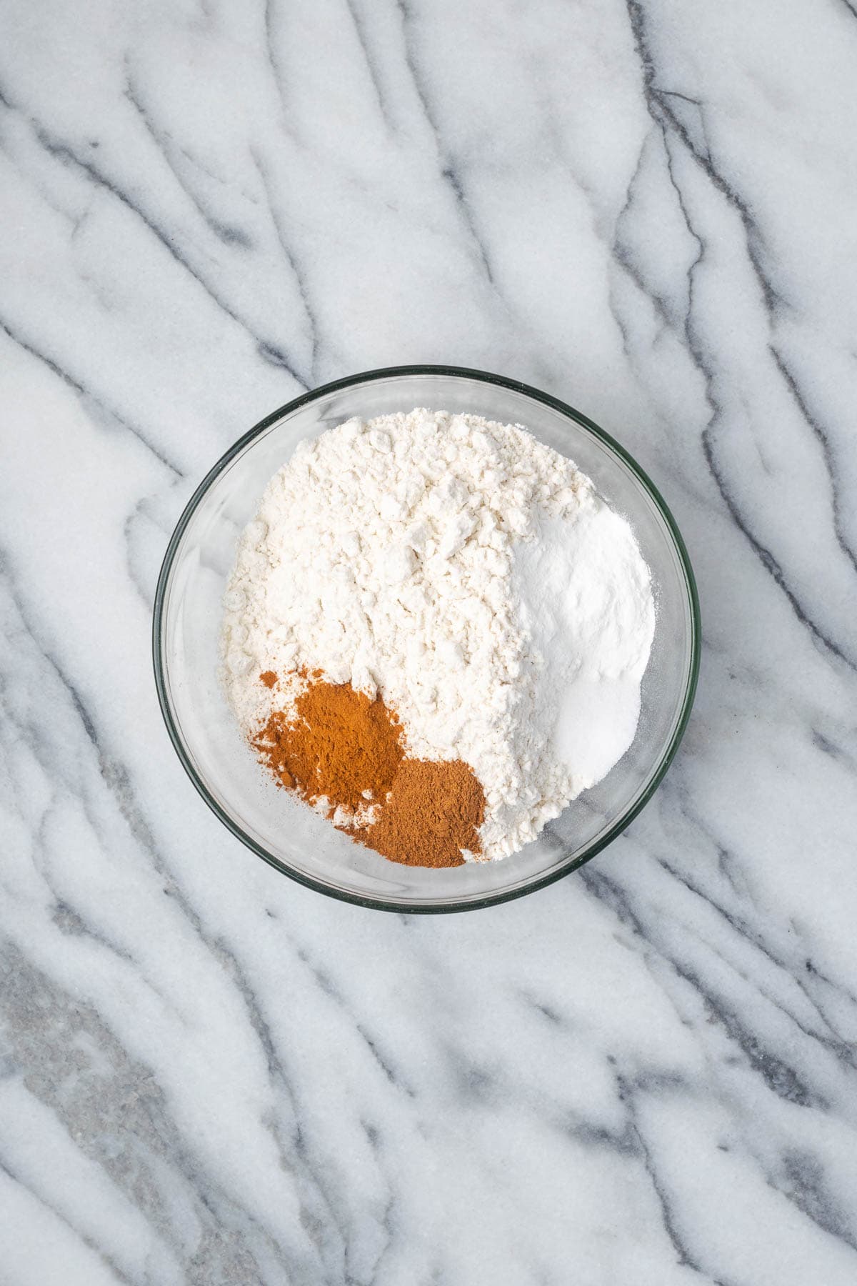 Flour, baking powder, salt, cinnamon and pumpkin pie spice combined in a small glass bowl.
