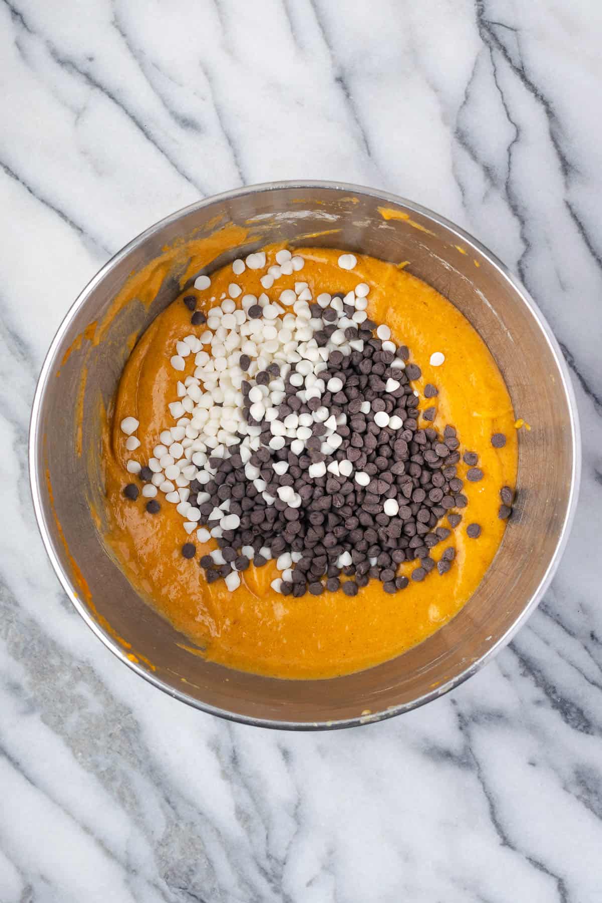 White chocolate chips and dark chocolate chips being stirred into the pumpkin cake batter.