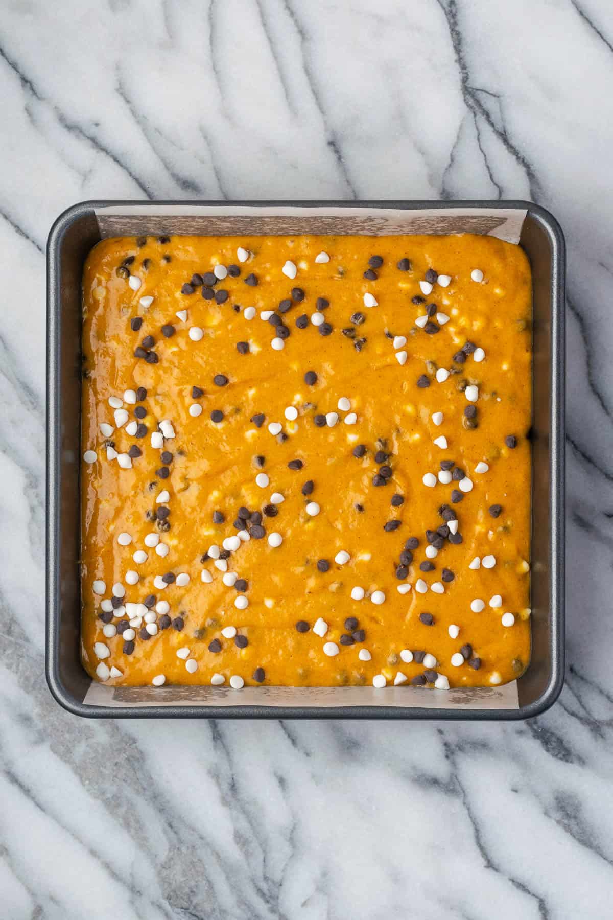 Unbaked pumpkin chocolate chip cake in a square pan sitting on a marble counter.