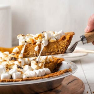 A slice of marshmallow topped sweet potato pie being lifted from a pie plate.