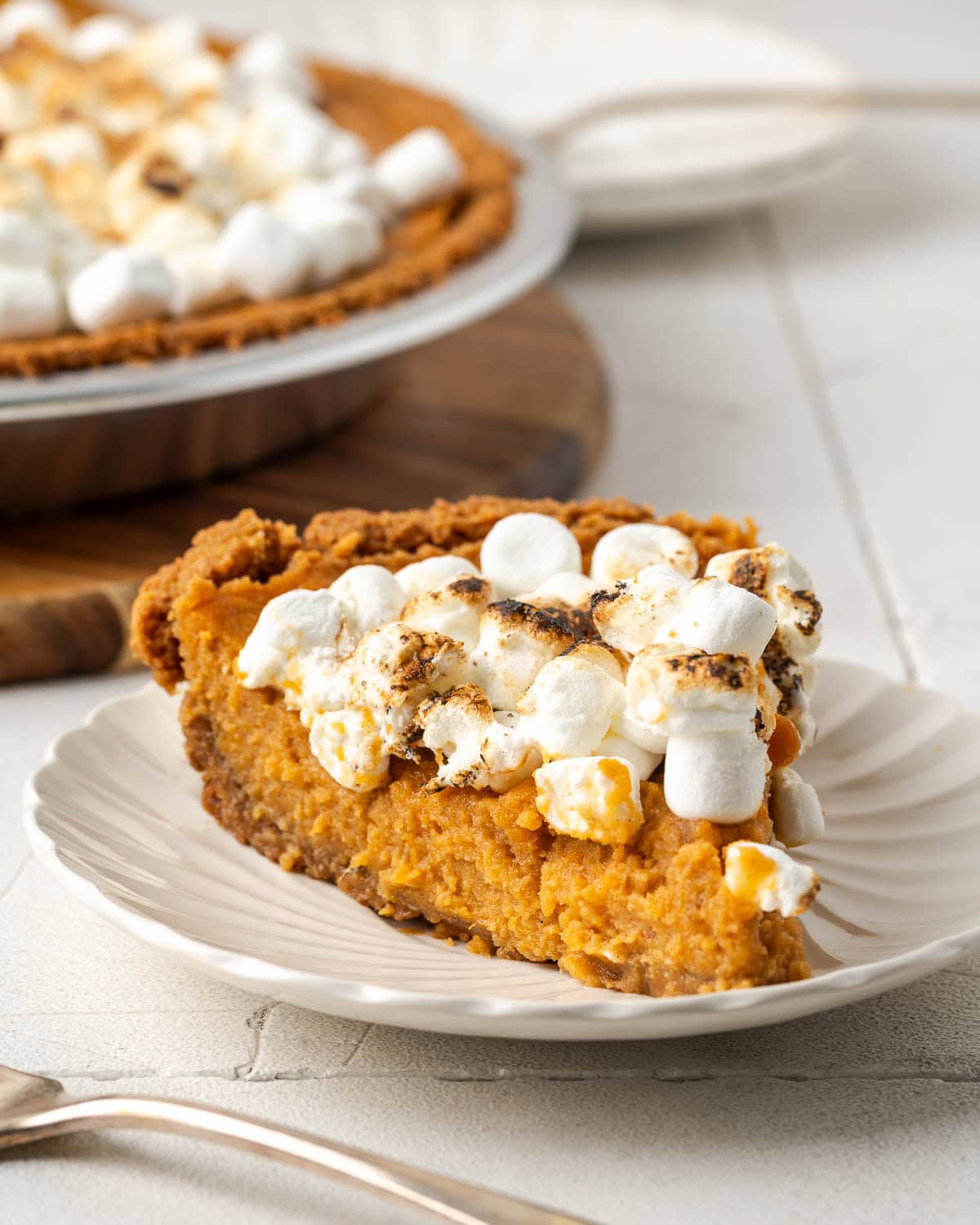 A slice of sweet potato pie topped with toasted marshmallows sitting on a small dessert plate. 