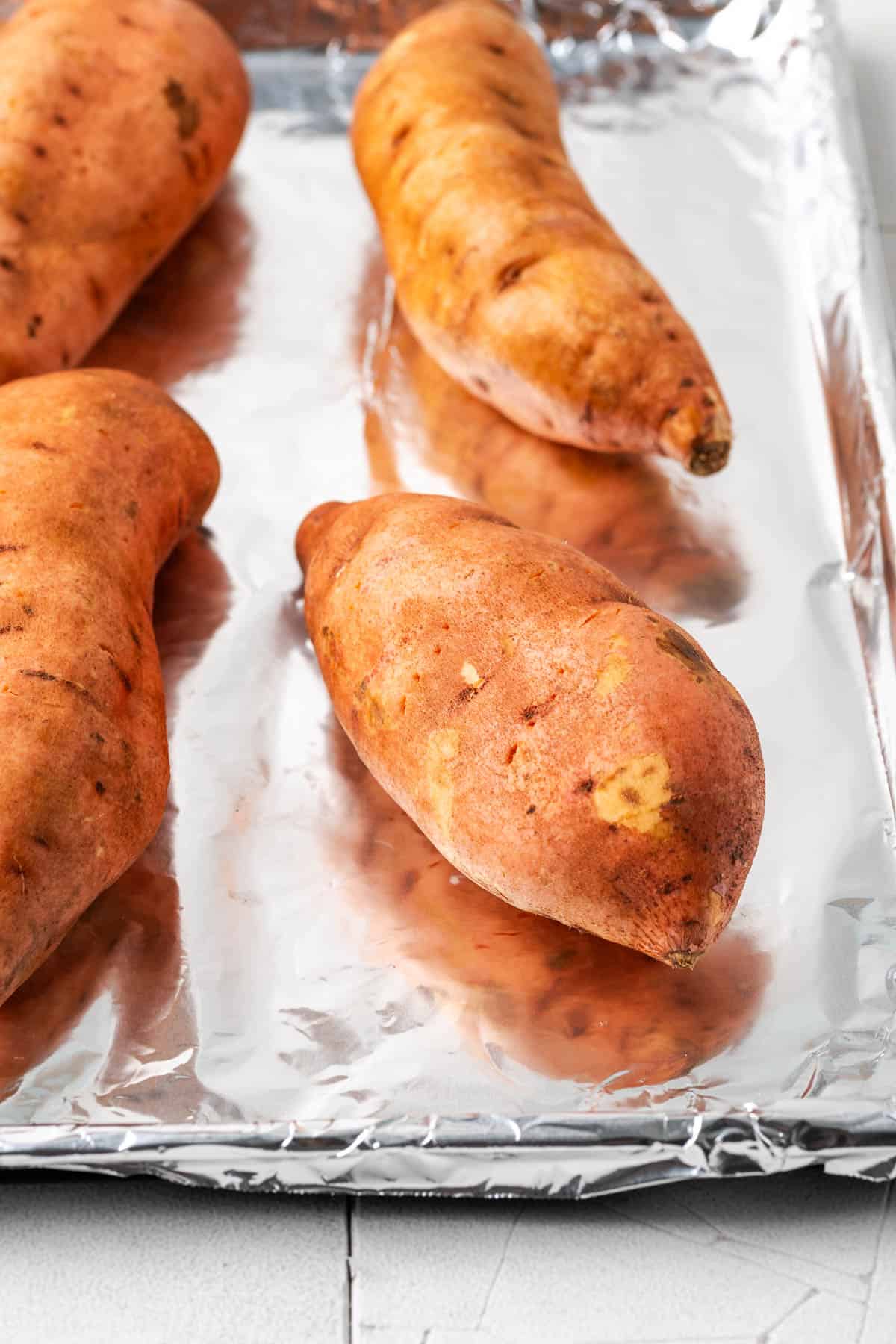 Several sweet potatoes on a baking pan lined with aluminum foil. 