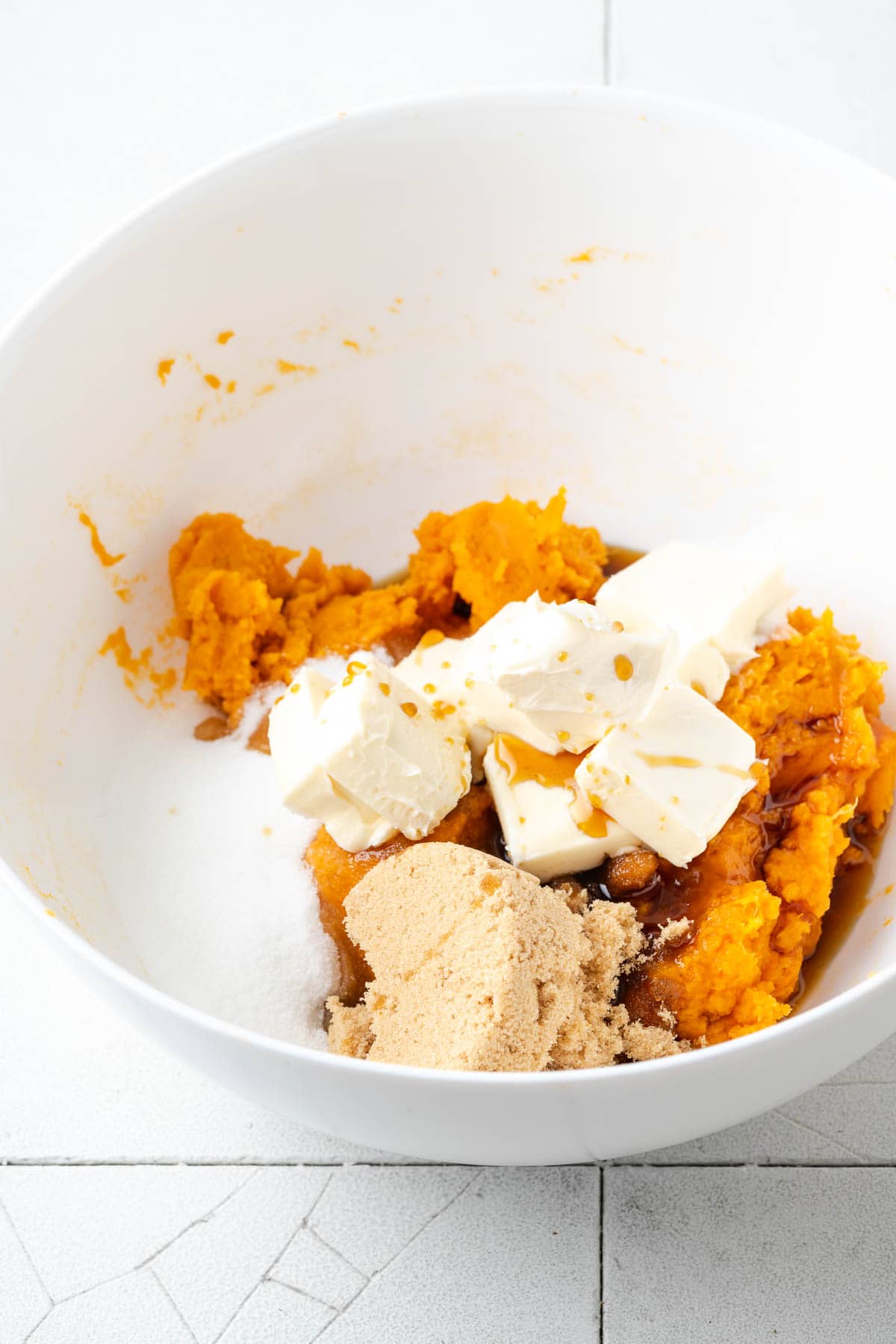 Sugar, brown sugar, butter, and maple syrup added to the bowl with the mashed sweet potatoes. 