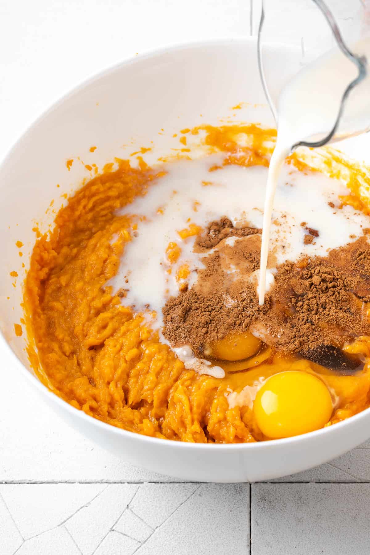 Milk, eggs, vanilla, cinnamon, salt and nutmeg being mixed into the pie filling. 