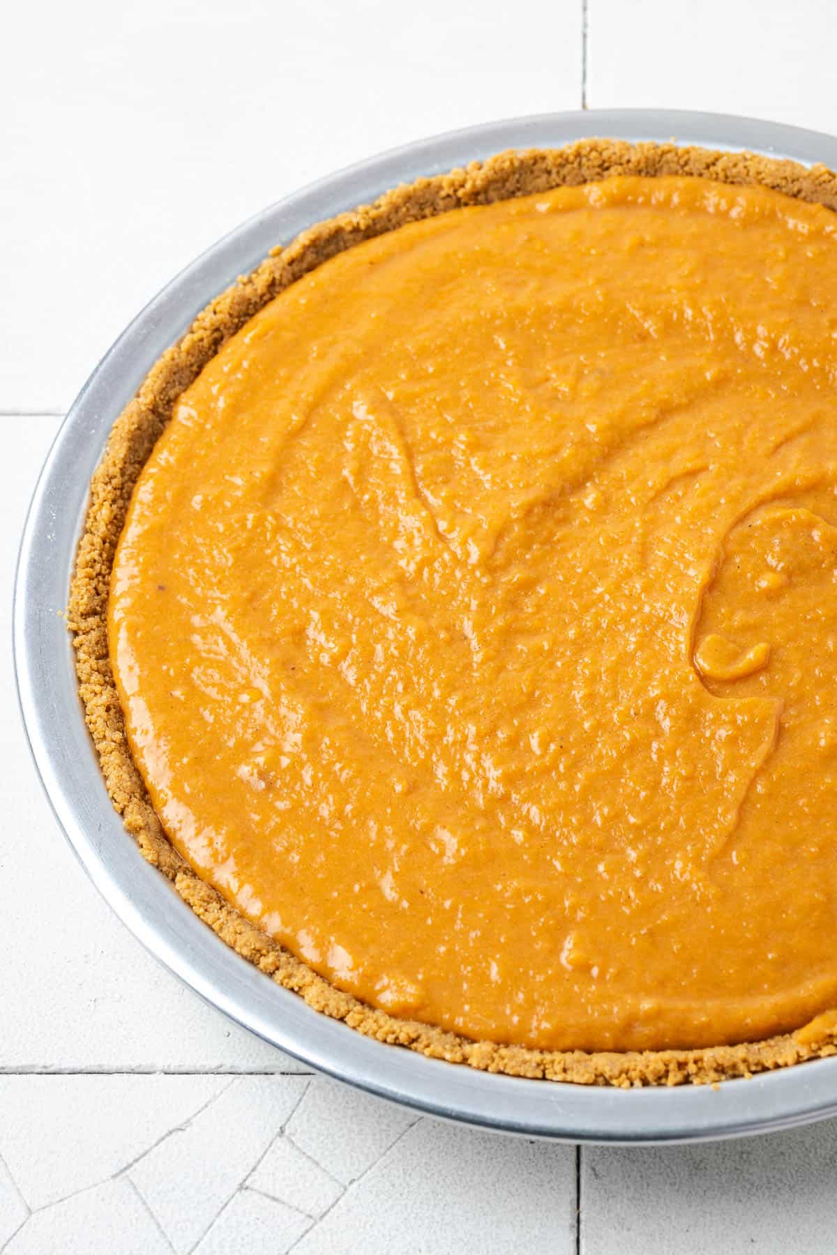An unbaked sweet potato pie sitting on a tile counter. 