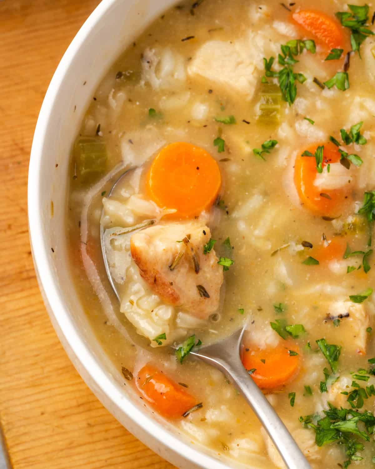 A spoon scooping up a bite of turkey and rice soup from a serving bowl.