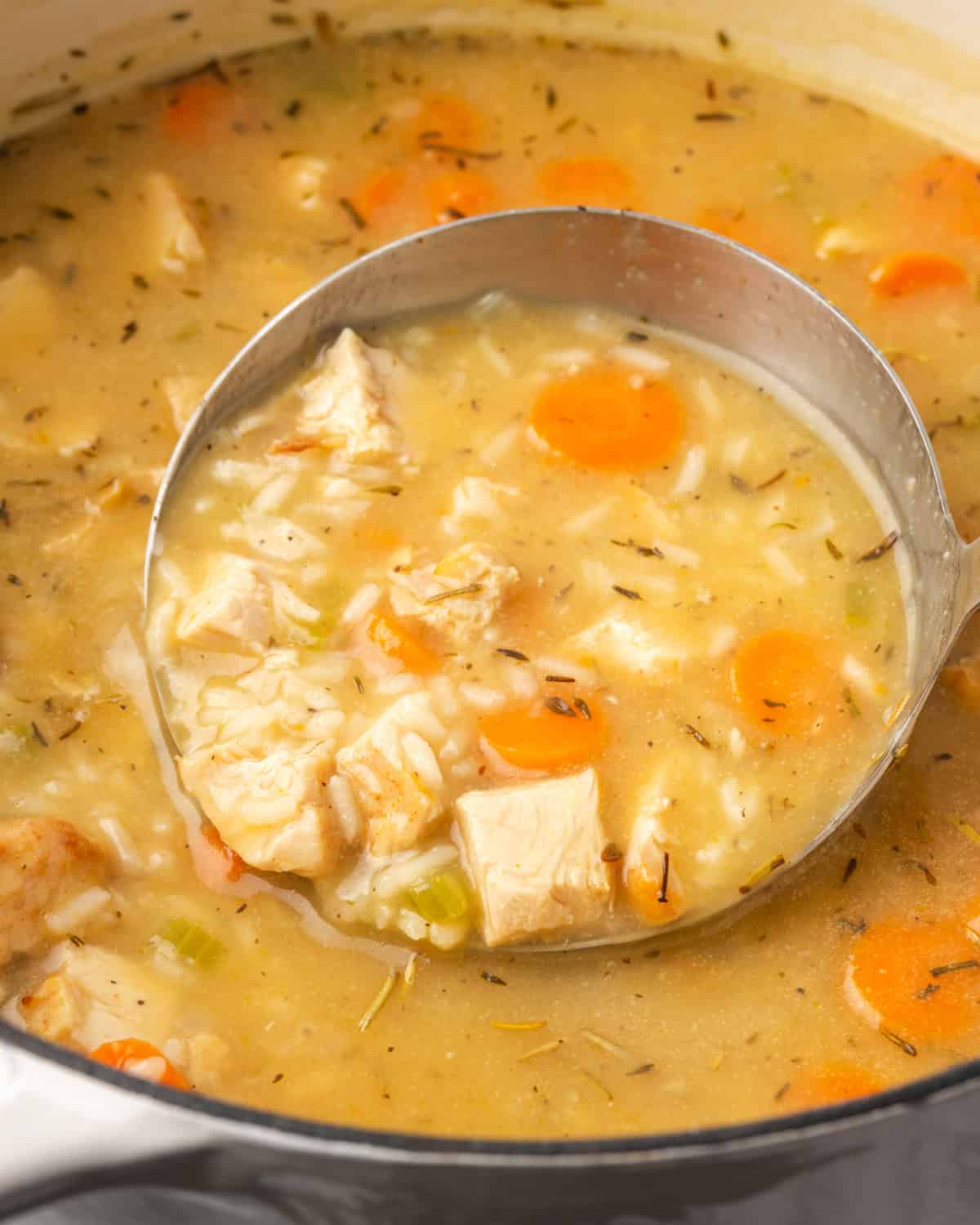 A soup ladle scooping a serving of turkey and rice soup from a large pot.