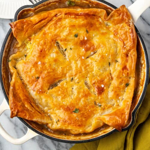 A turkey pot pie topped with puff pastry in a cast iron skillet.