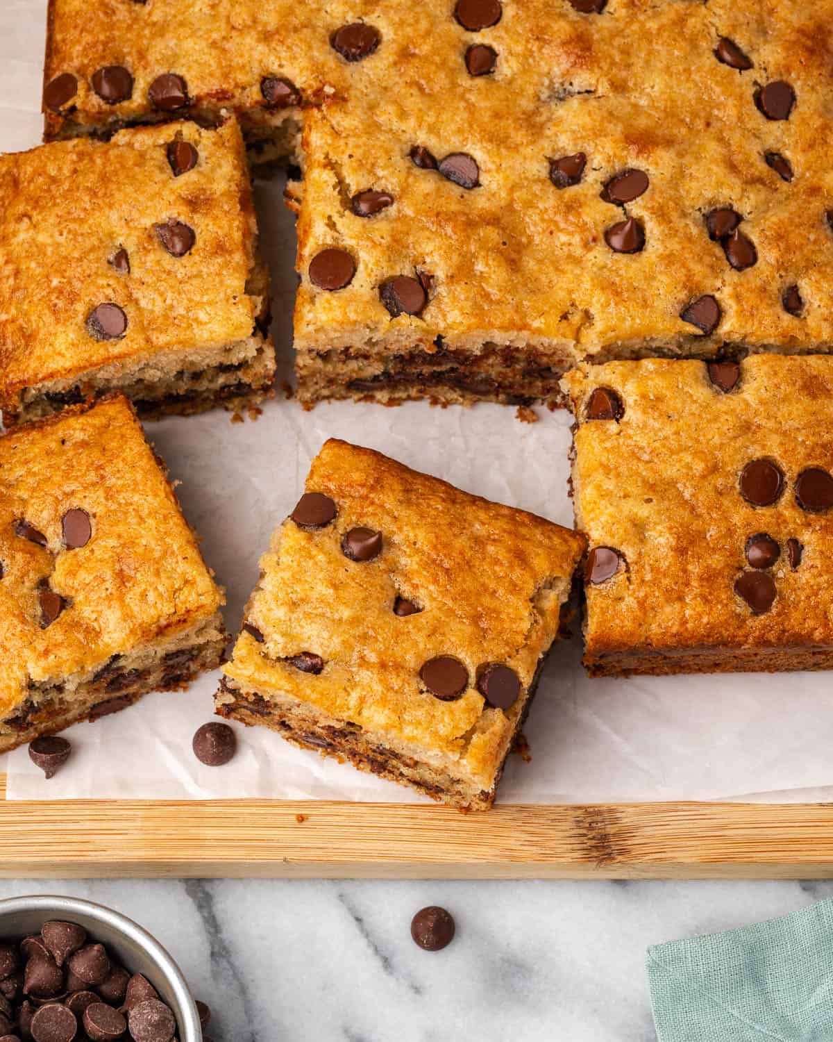 A banana chocolate chip cake cut into square pieces sitting on a wood board. 