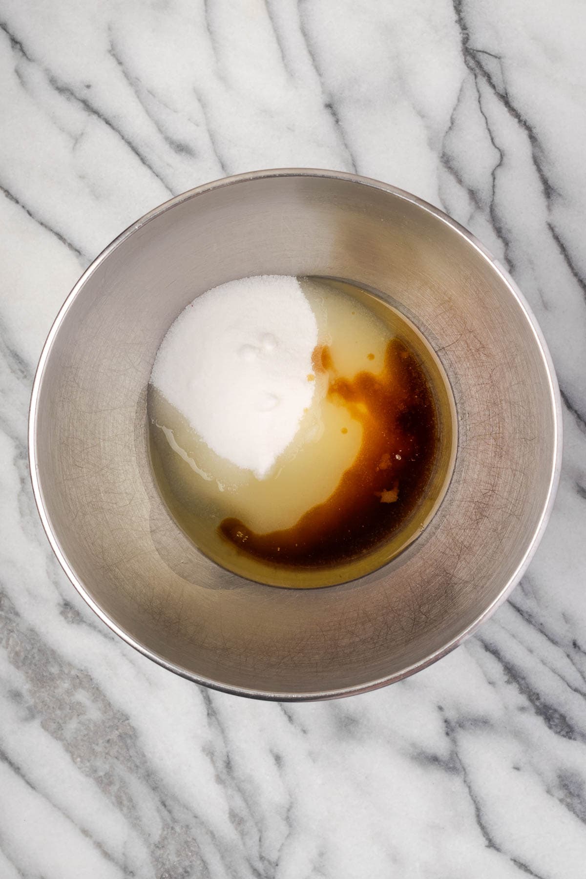 Sugar, maple syrup and oil combined in a large metal mixing bowl. 