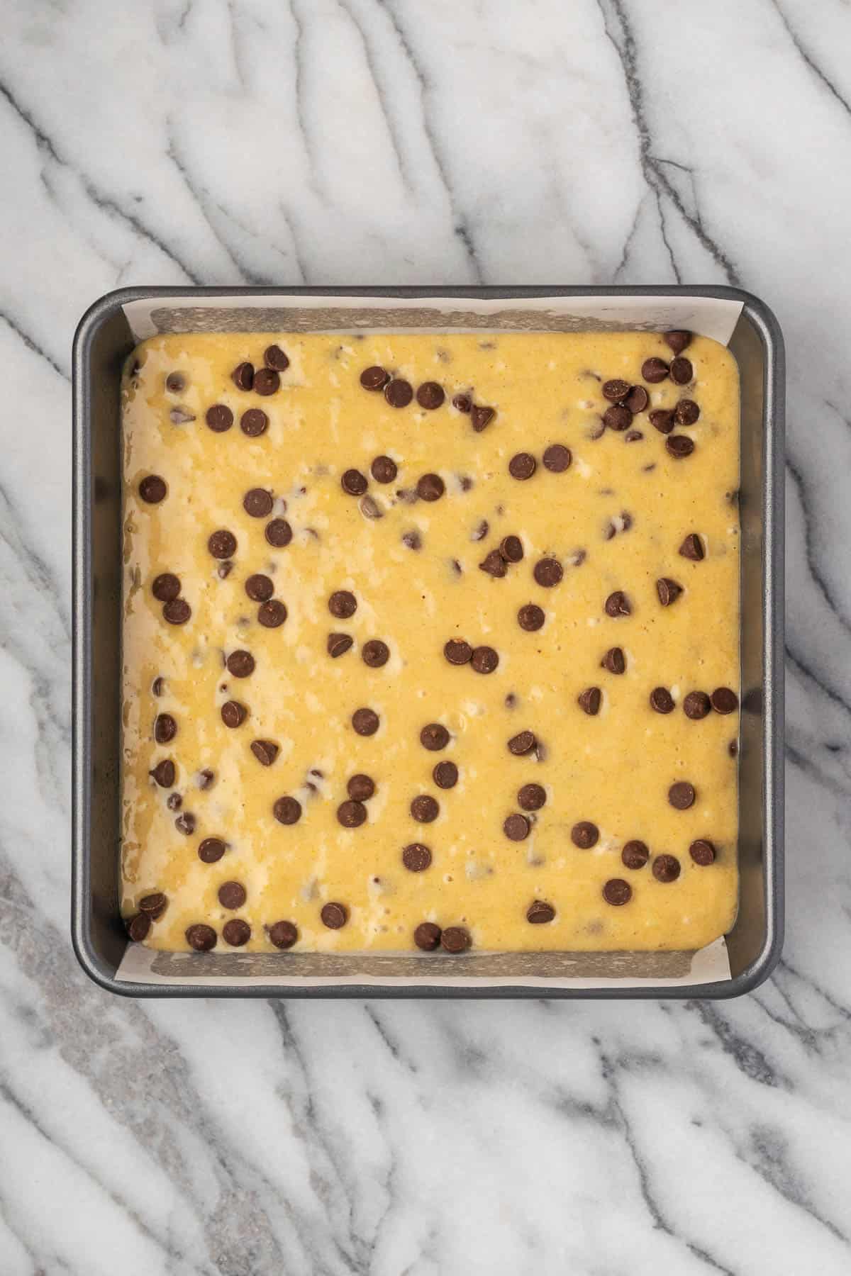 An unbaked banana chocolate chip cake in a square baking pan. 