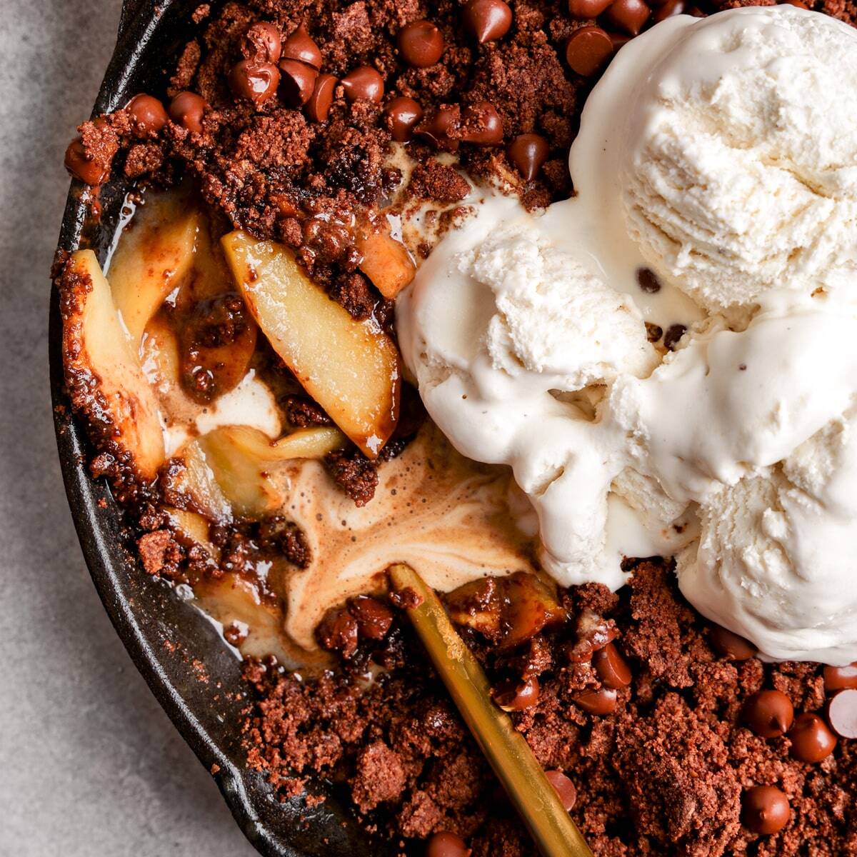 A baked apple crisp topped with a chocolate crumble topping, chocolate chips and scoops of vanilla ice cream.