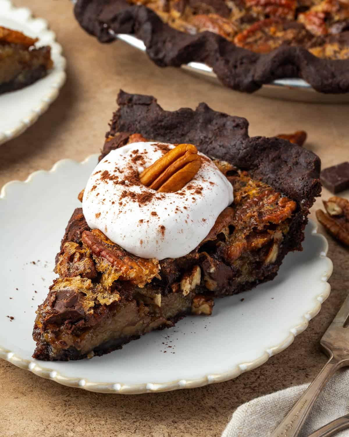 A slice of chocolate pecan pie topped with whipped cream sitting on a small dessert plate.