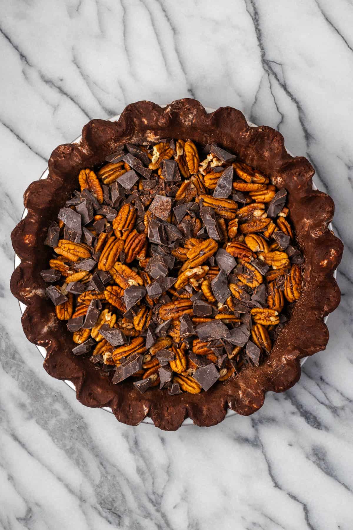 Pecans and chopped chocolate spread in the bottom of an unbaked pie shell.