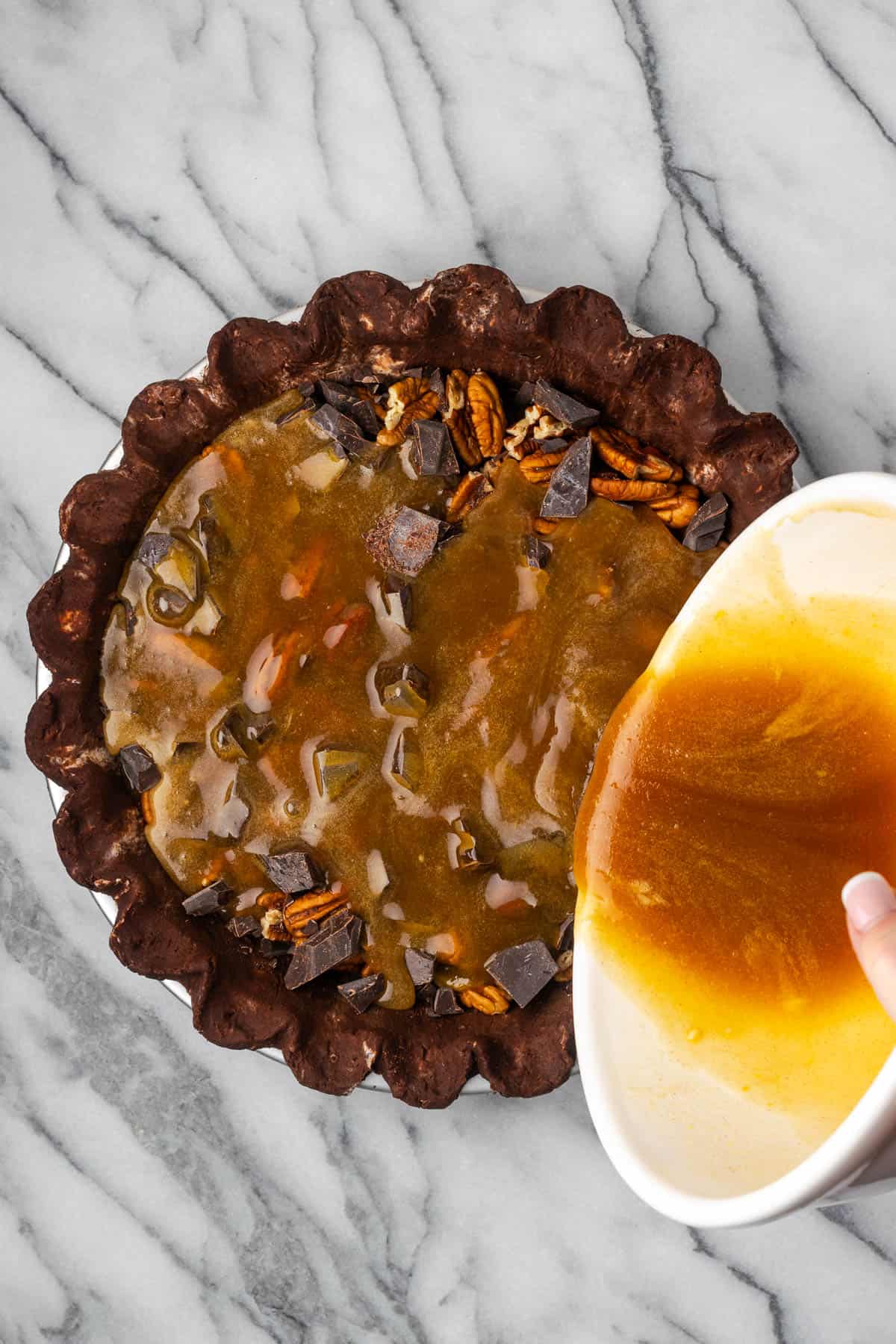 Pecan pie filling being poured over the nuts and chocolate.
