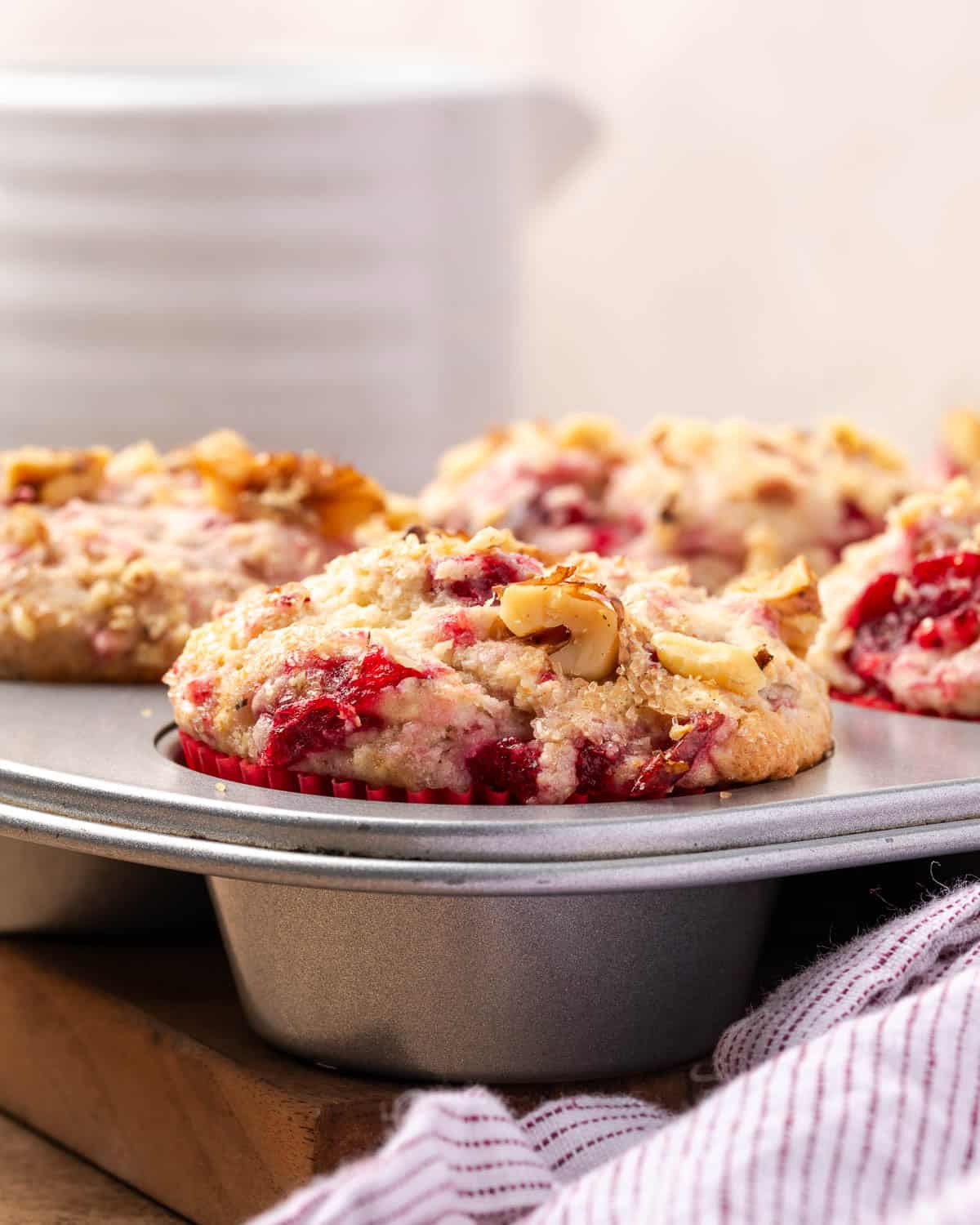A batch of freshly baked cranberry sauce muffins in a metal baking tin sitting on a counter.