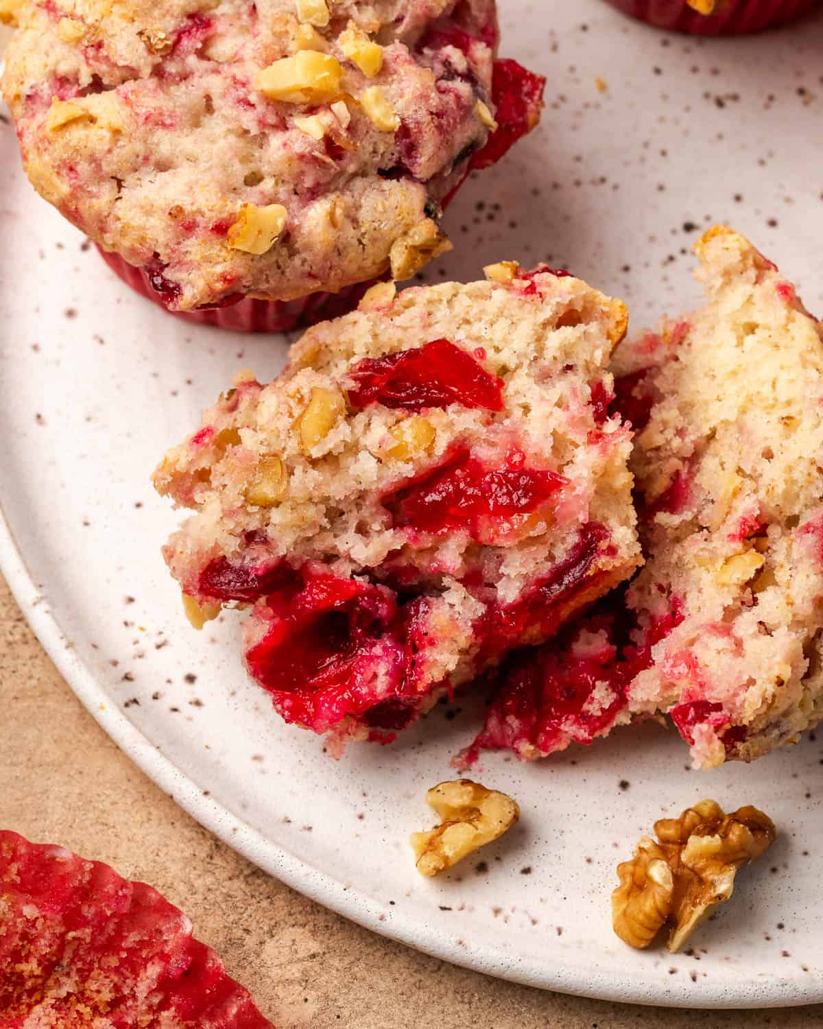 A cranberry sauce muffin cut in half showing pieces of cranberry and walnuts inside.
