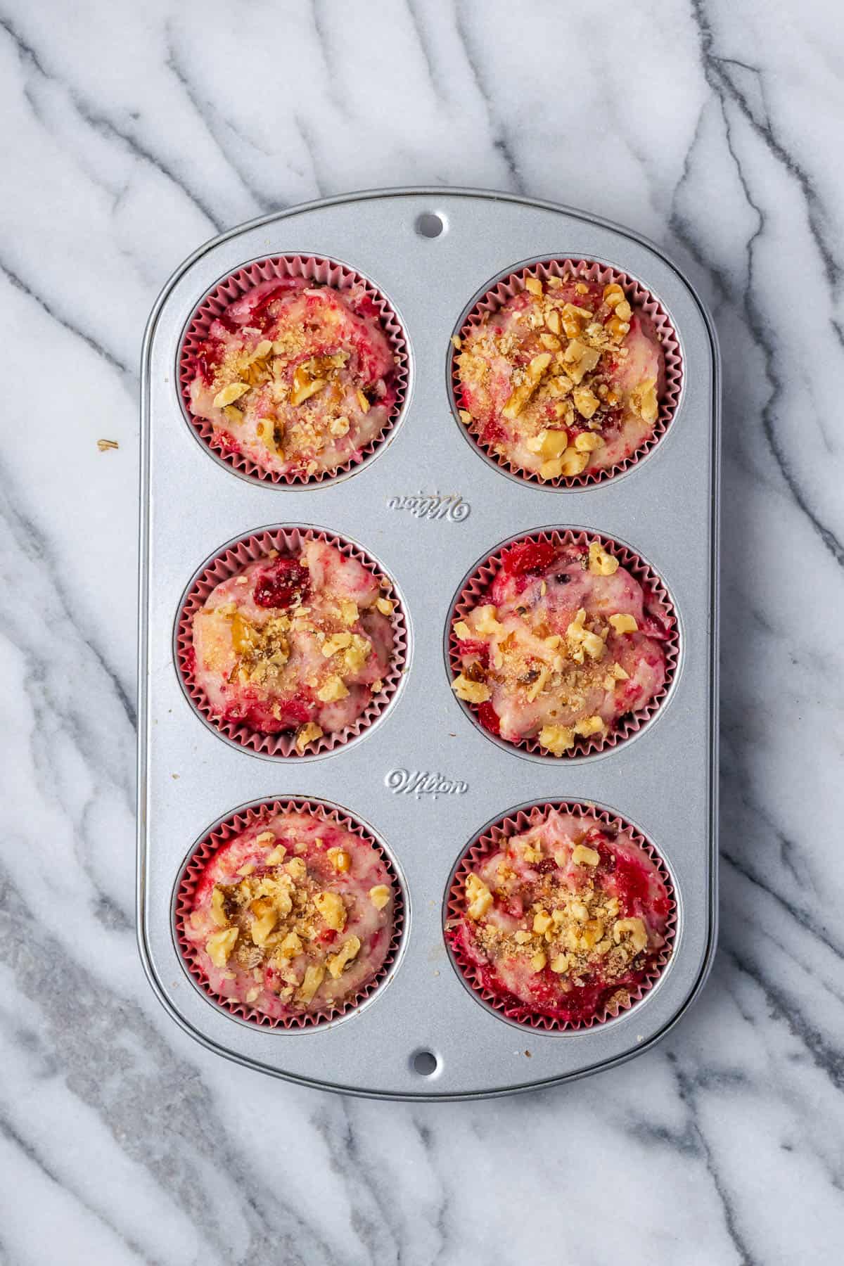 A muffin tin filled with unbaked cranberry sauce muffin batter.